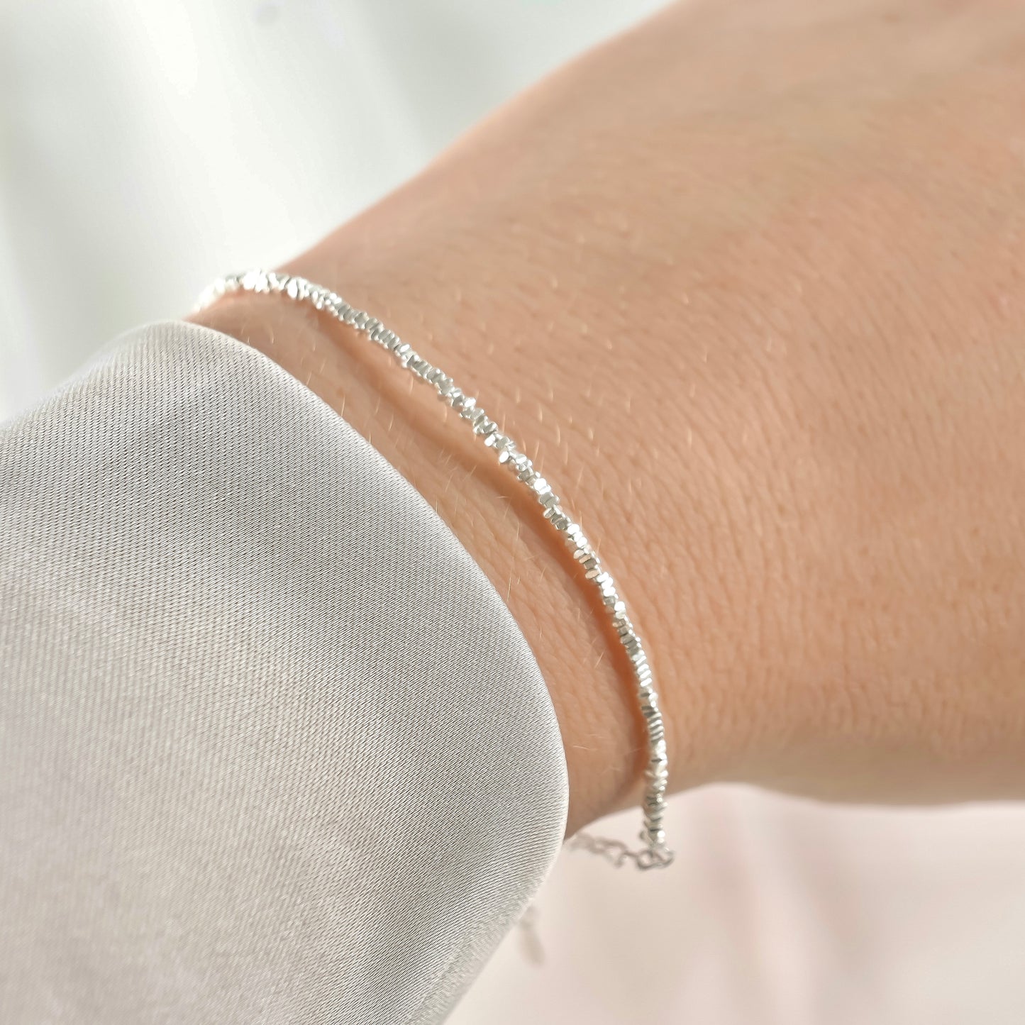 Silver beaded chain bracelet on a wrist under direct sunlight