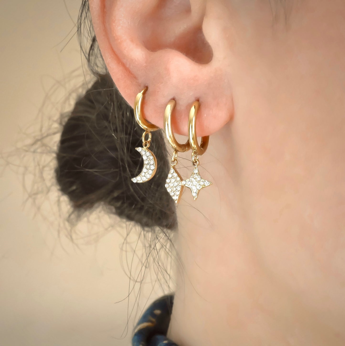 Close up view of Stacked spark, rhombus and crescent moon dangle hoops with clear diamond accents on a person's ear.