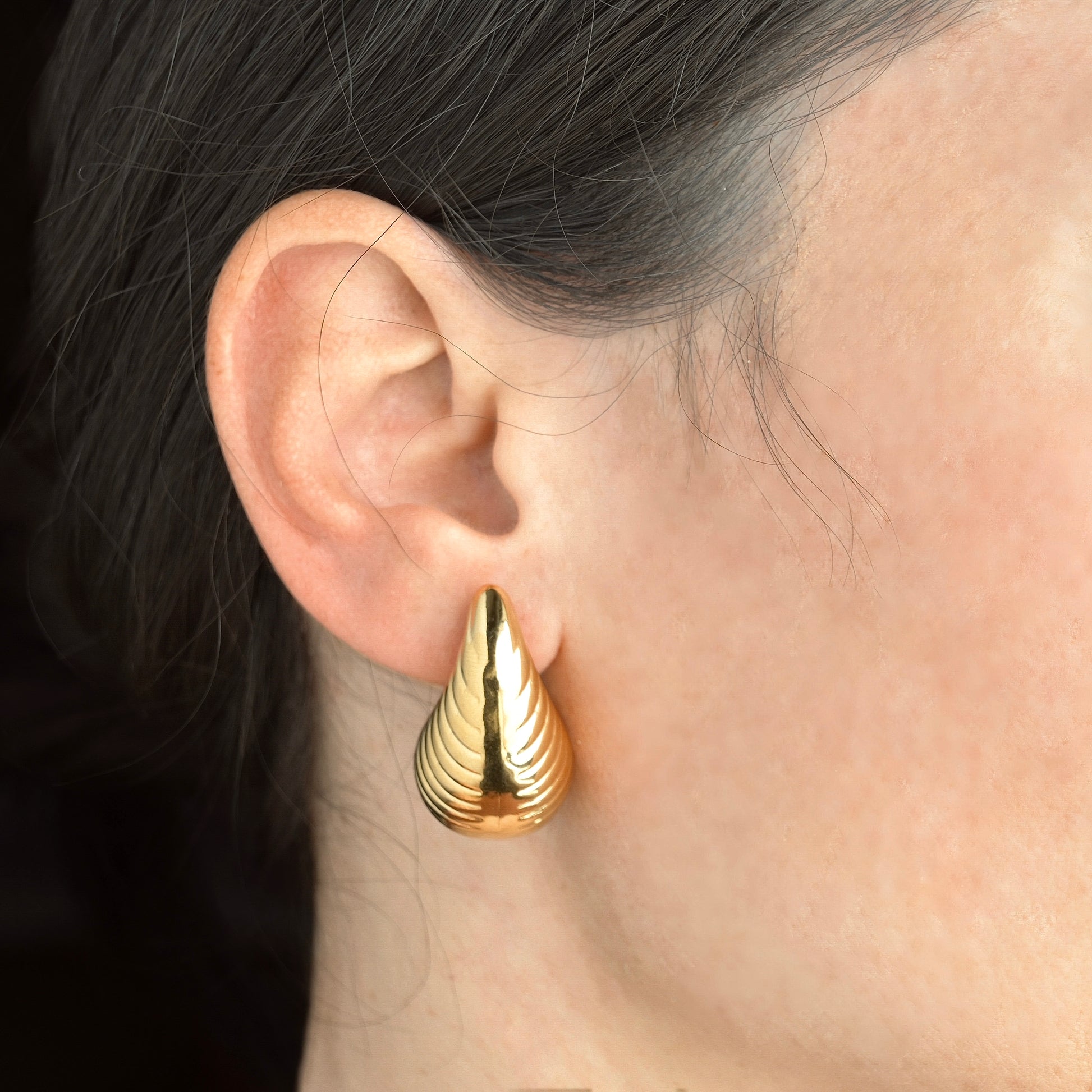 Gold ribbed pear drop earrings worn by a person with dark hair.