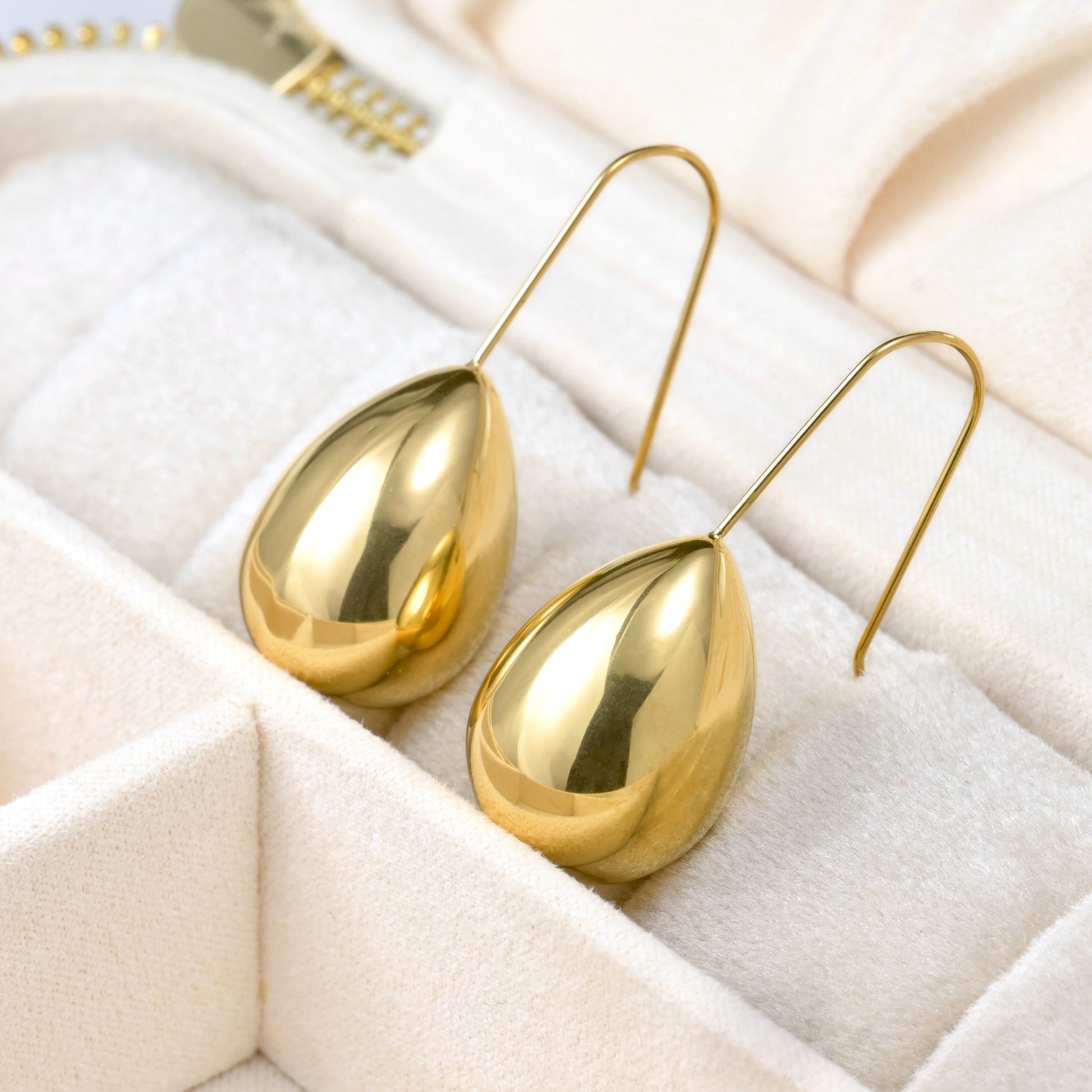 Gold teardrop earrings on a white quilted surface