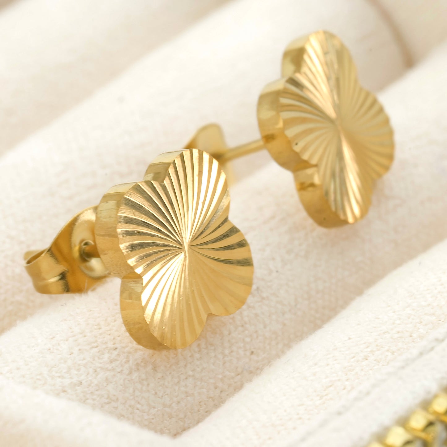 Gold leaf-shaped earrings  with sunburst texture on a white cushion