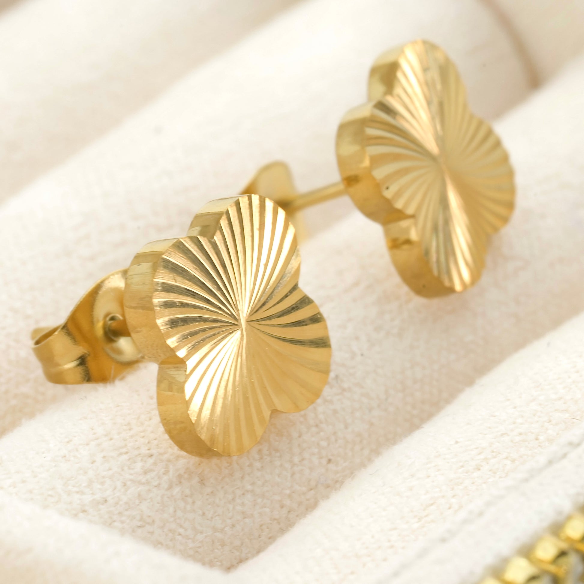 Gold leaf-shaped earrings  with sunburst texture on a white cushion