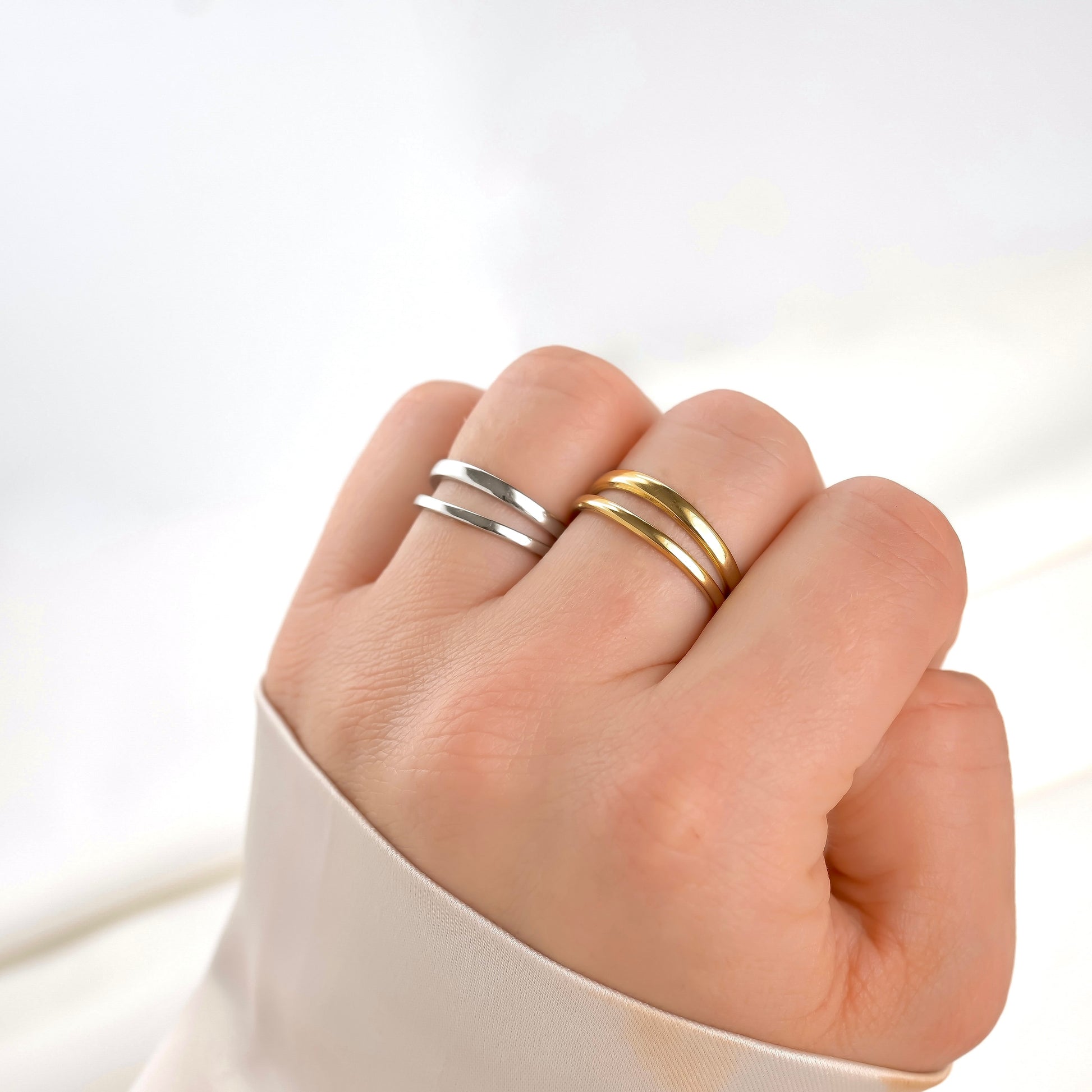 Fist pose of Hand wearing two layered rings, one gold and one silver, on a white background