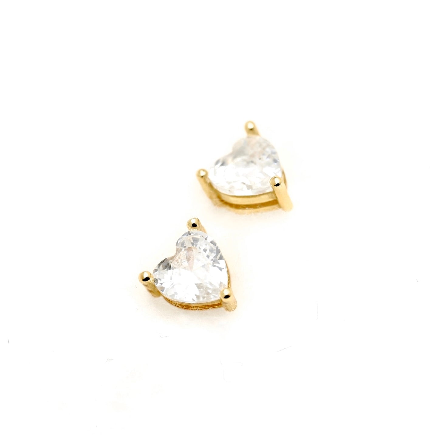 A pair of gold heart-shaped stud earrings with clear heart-cut gemstones, set against a plain white background.