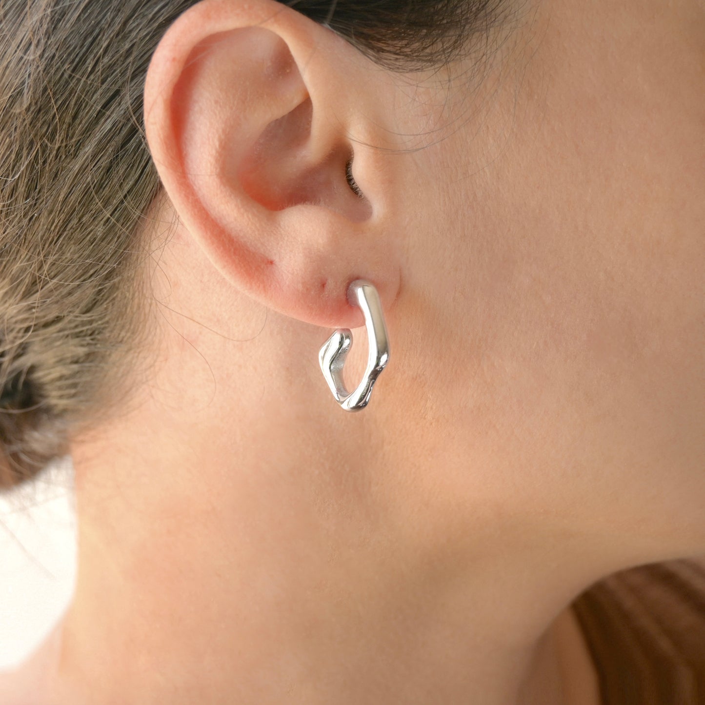 Silver fluid hoop earring worn by a person with a neutral background