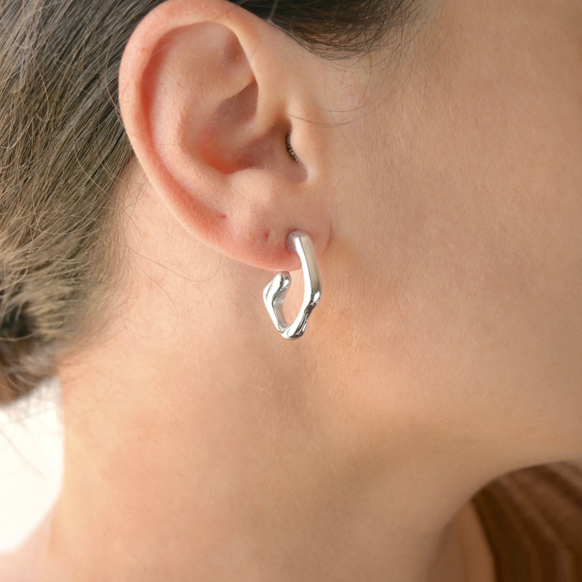 Silver fluid hoop earring worn by a person with a neutral background