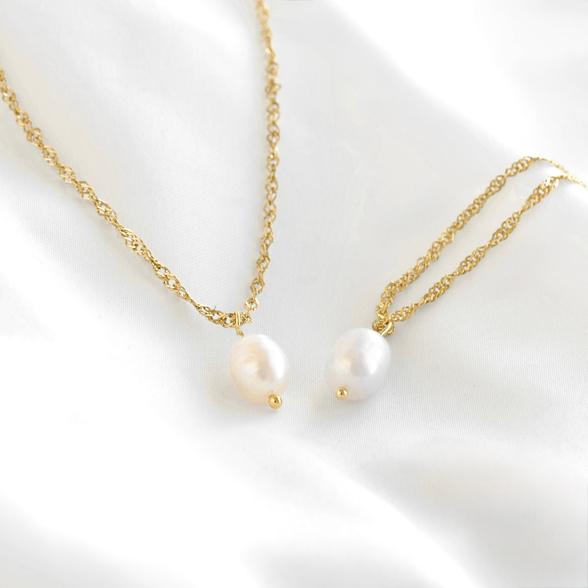 Two delicate gold chain necklace and bracelet with irregular white freshwater pearls, displayed on a soft white satin fabric background.