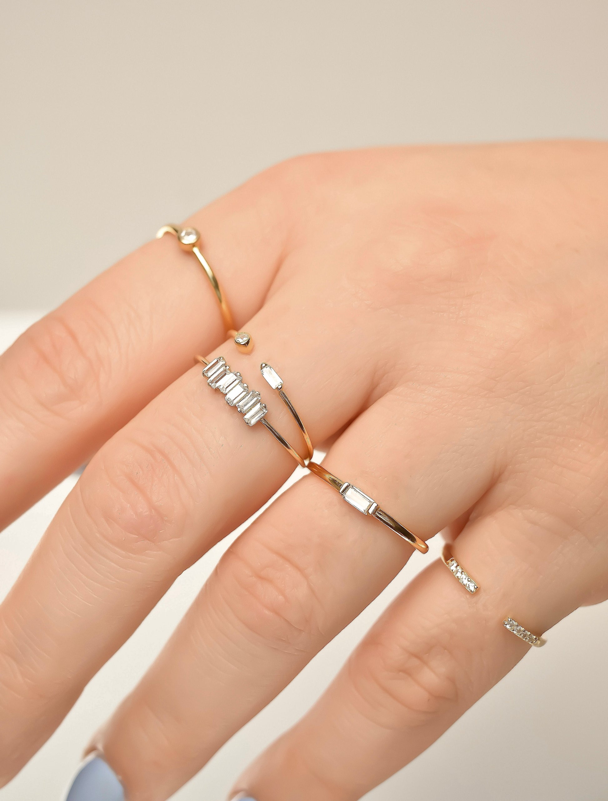 Close-up of a hand wearing stacked gold rings on a neutral background