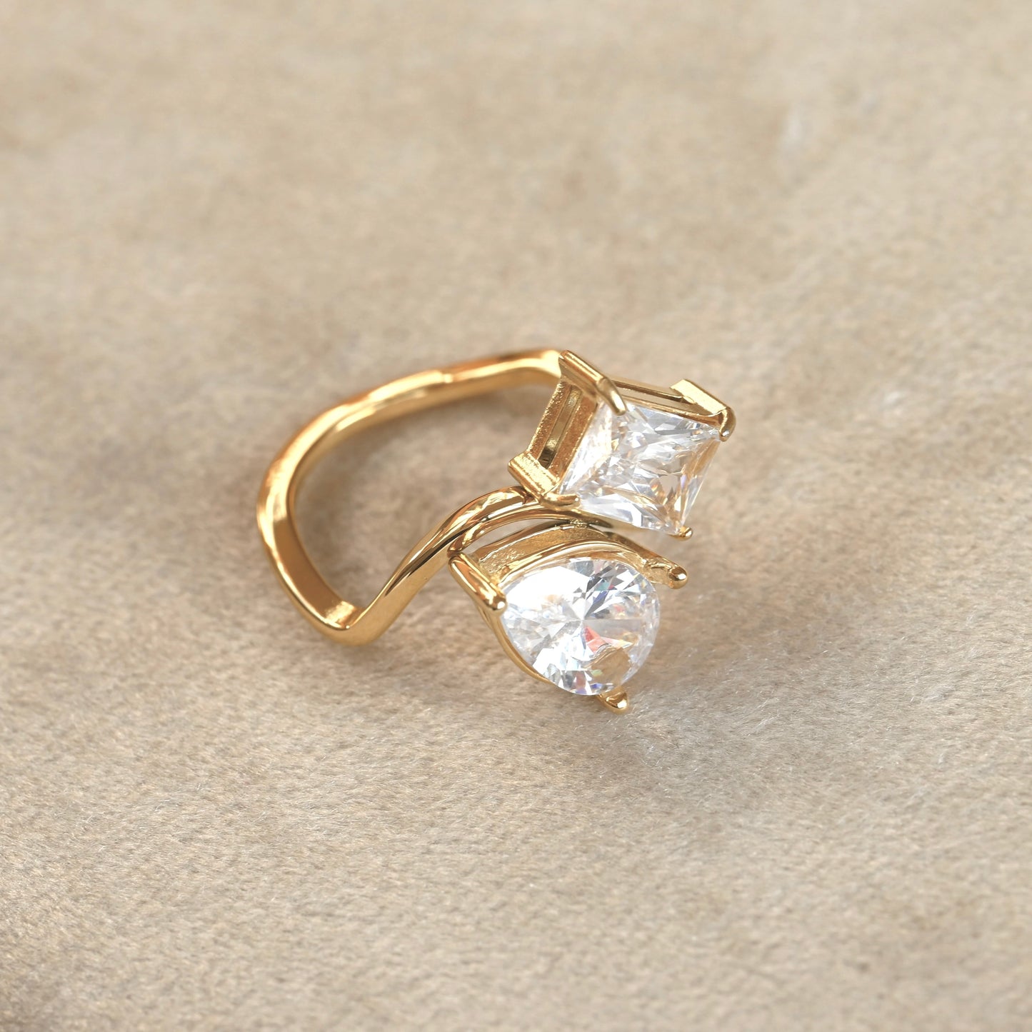 Gold coctail ring with two clear gemstones on a beige background