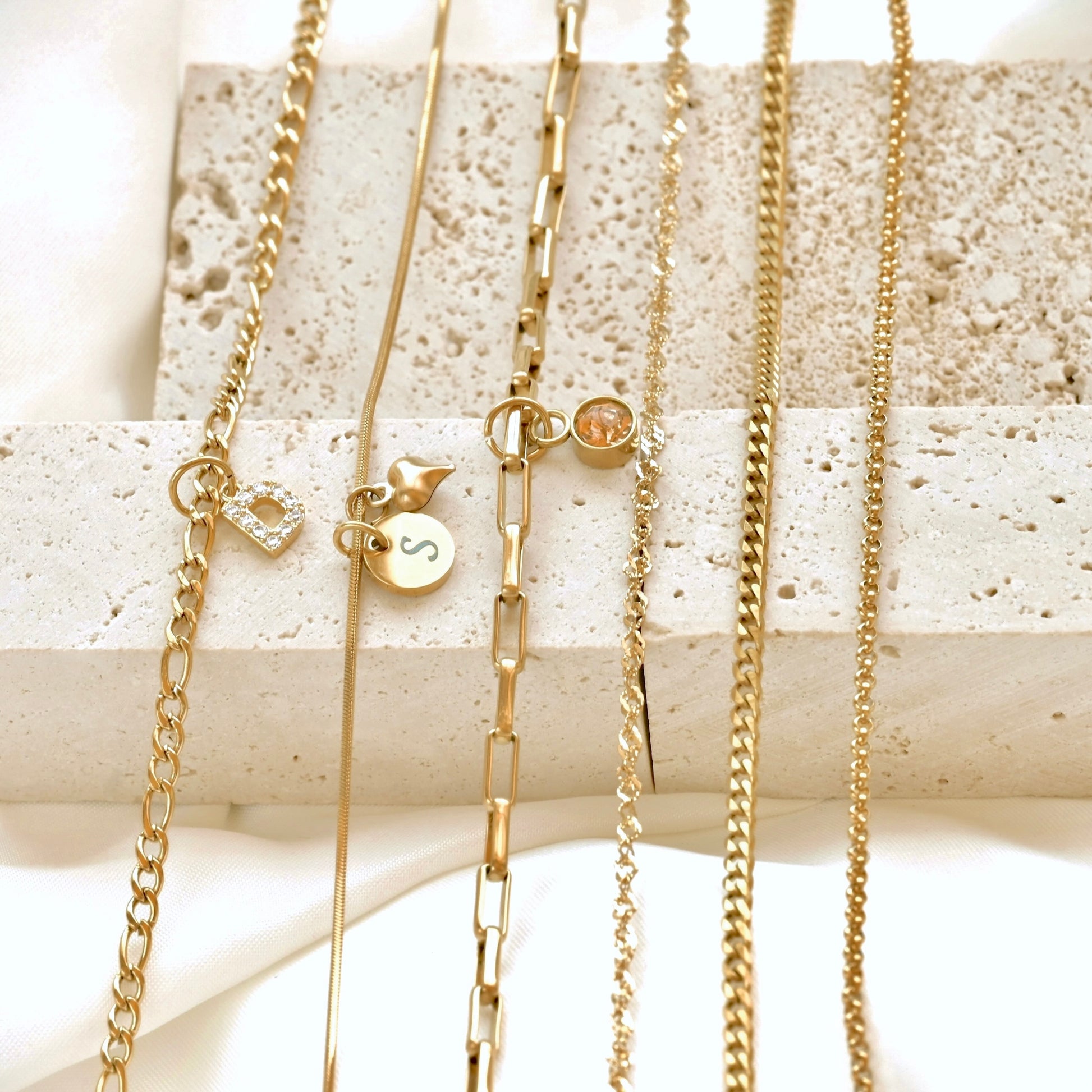 Stainless steel gold chains with various designs on a textured white surface