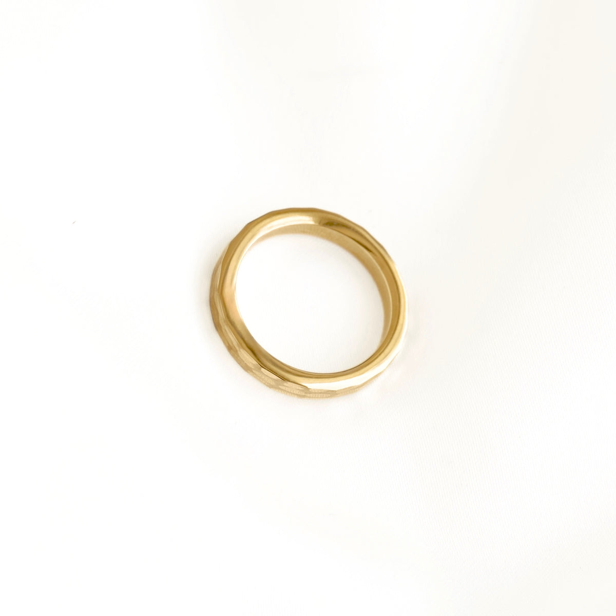A single gold ring with a textured, slightly angular band, photographed on a clean white background.
