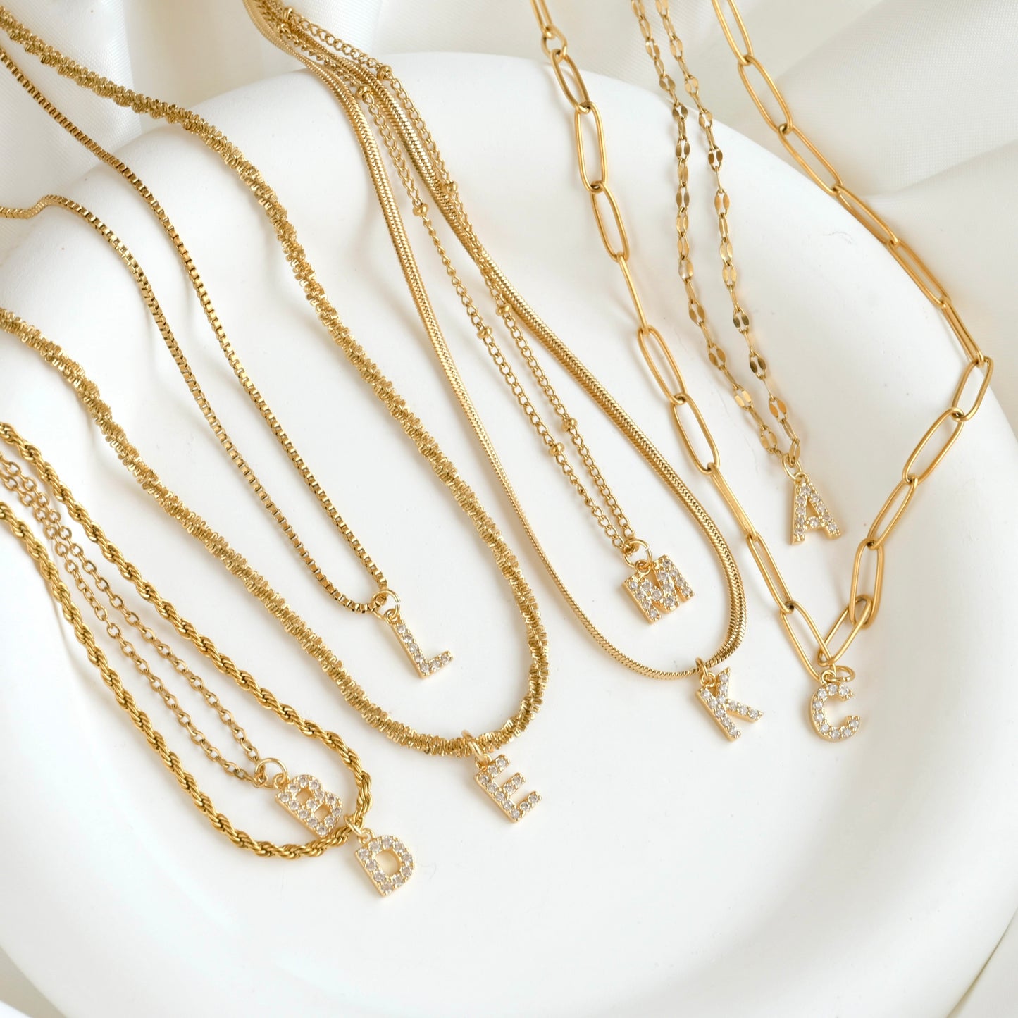 Top view of small pave CZ letter pendants on various chains on a white dish.
