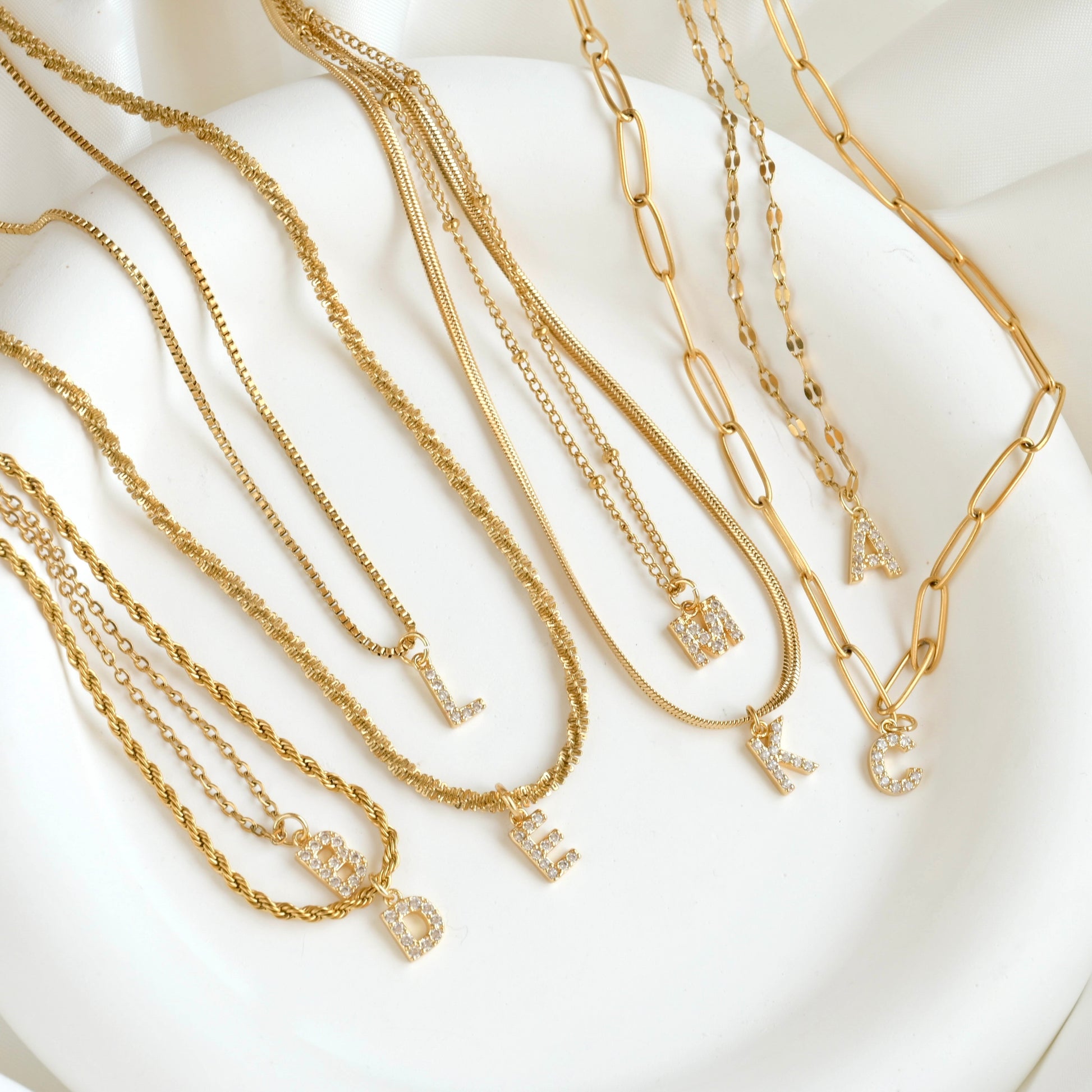 Top view of small pave CZ letter pendants on various chains on a white dish.