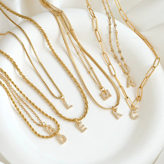 Top view of small pave CZ letter pendants on various chains on a white dish.