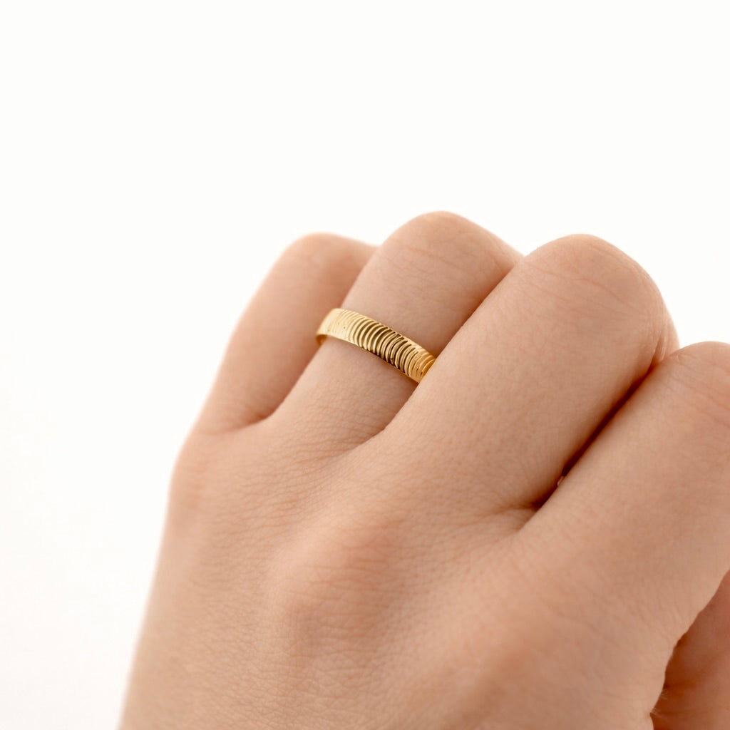 A close-up of a hand wearing a thin, textured gold band ring against a clean white background.