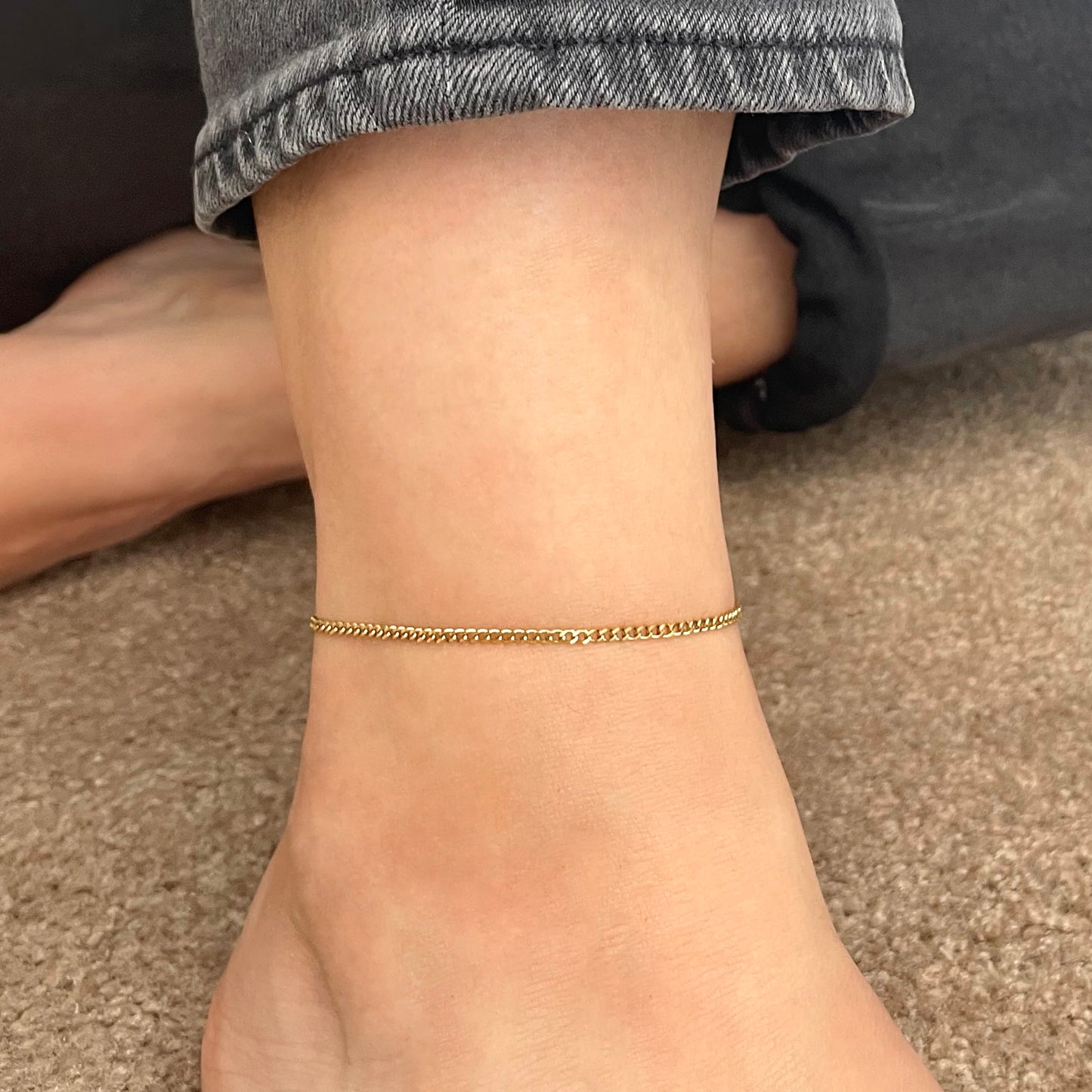 Dainty gold chain anklet on a person's ankle with a blurred background