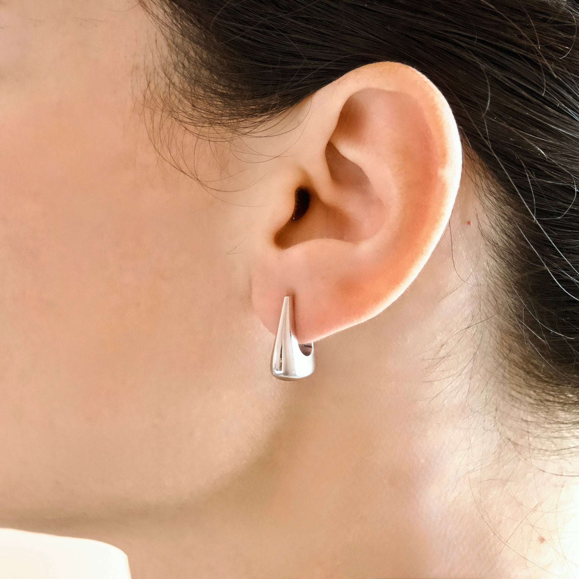 A close-up of a person's ear wearing a small chunky U-shaped silver hoop earring with a sharp triangular spike extending from the front.