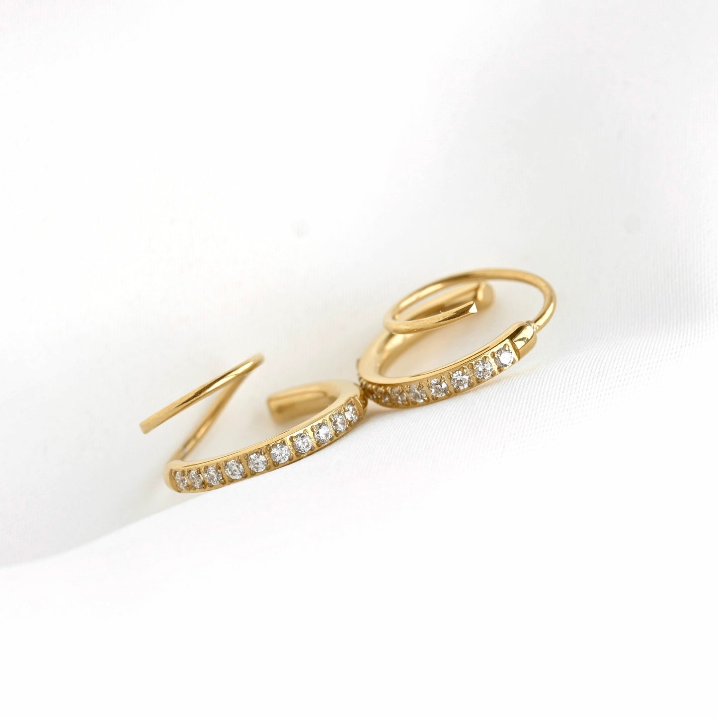 A pair of gold spiral hoop earrings with rows of small clear stones, displayed on a clean white background.