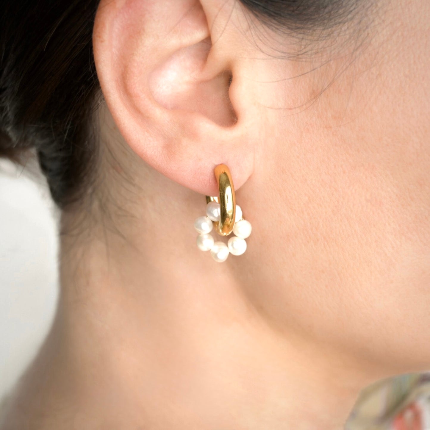 Gold tunnel hoop earring with pearl cluster  circle charm worn by a person