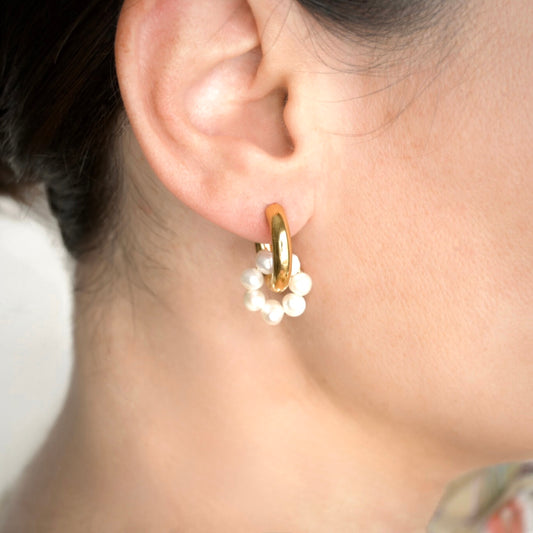 Gold tunnel hoop earring with pearl cluster  circle charm worn by a person