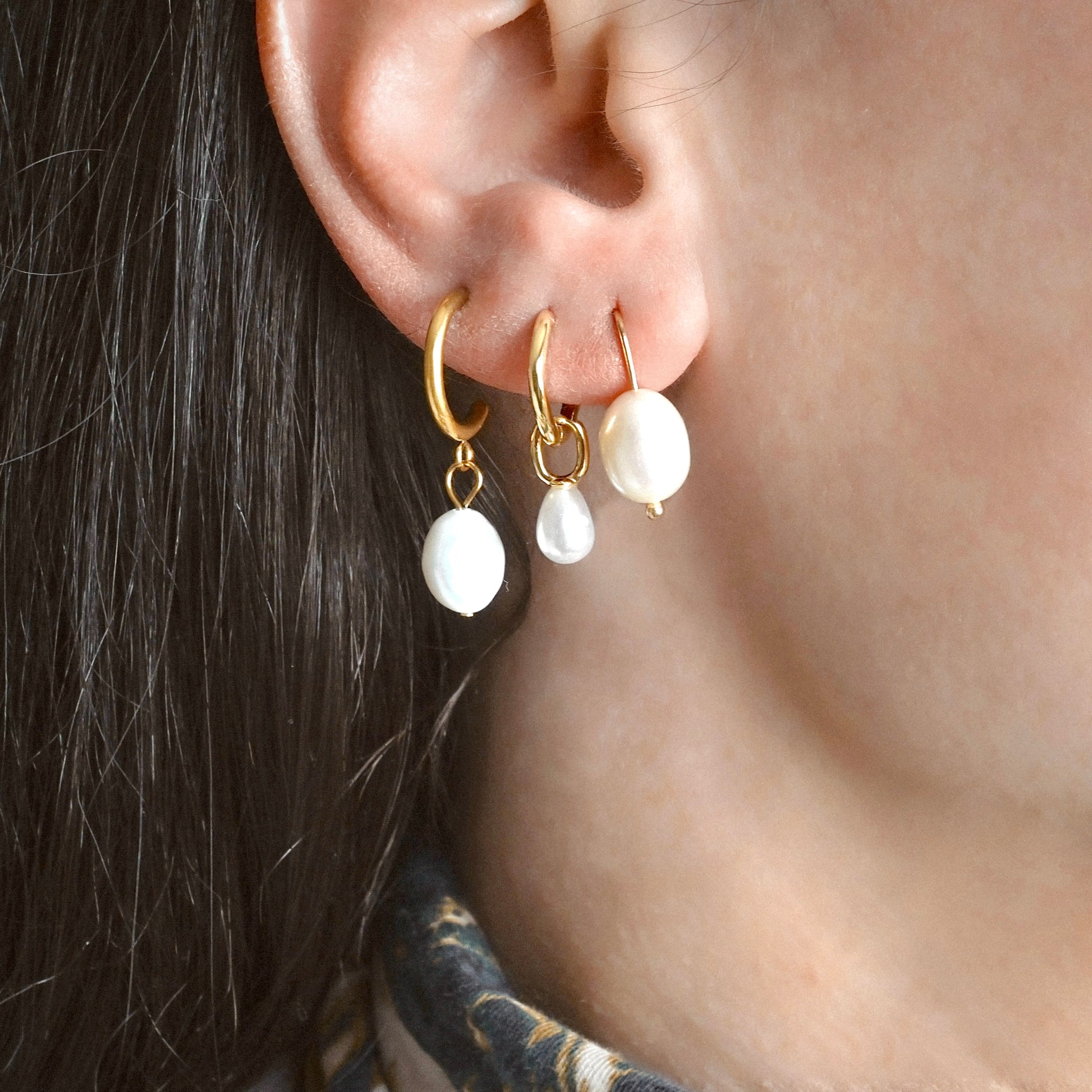 Close-up of an ear wearing gold hoop earrings with white pearl charms.