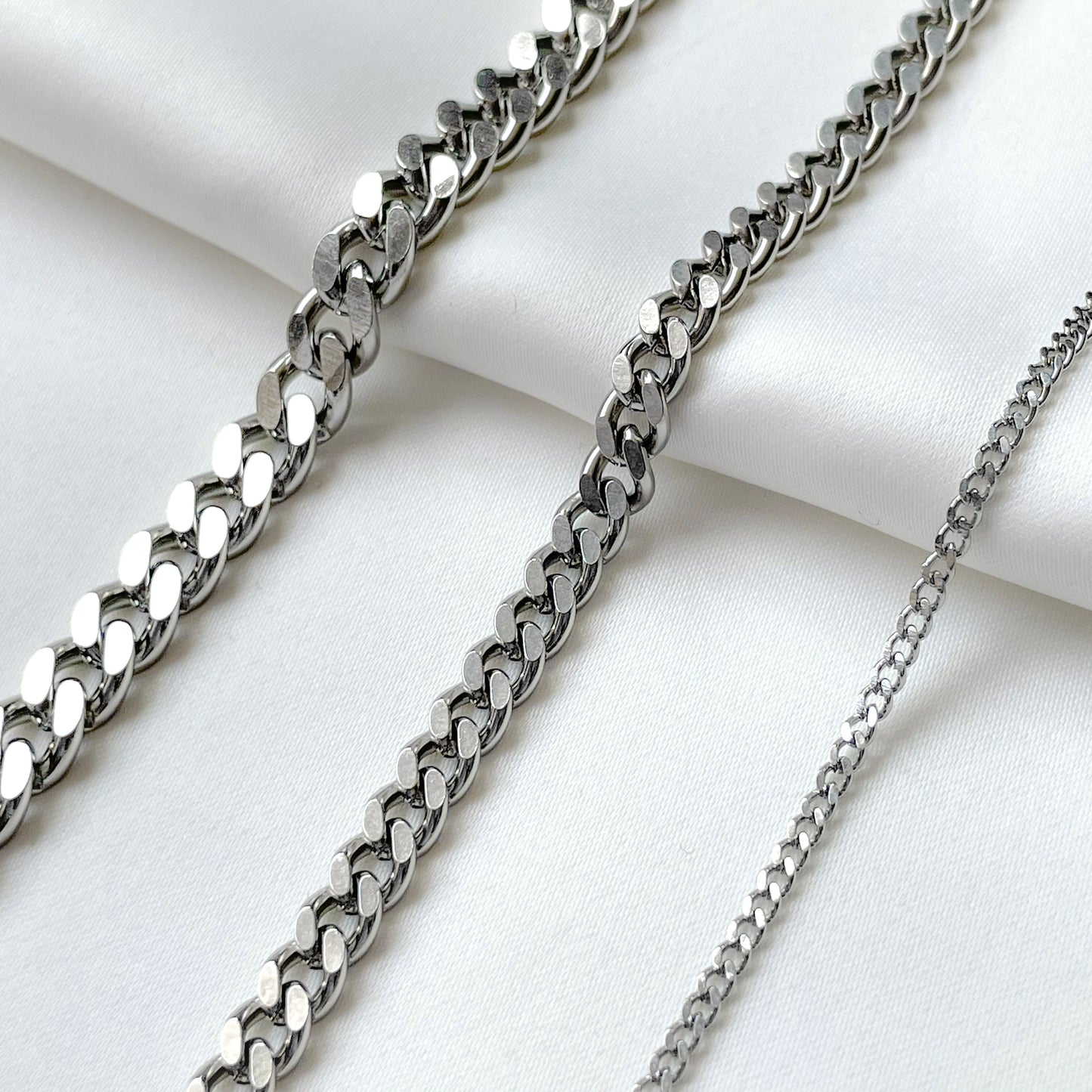 Three silver cuban bracelets in various thicknesses on a white fabric background