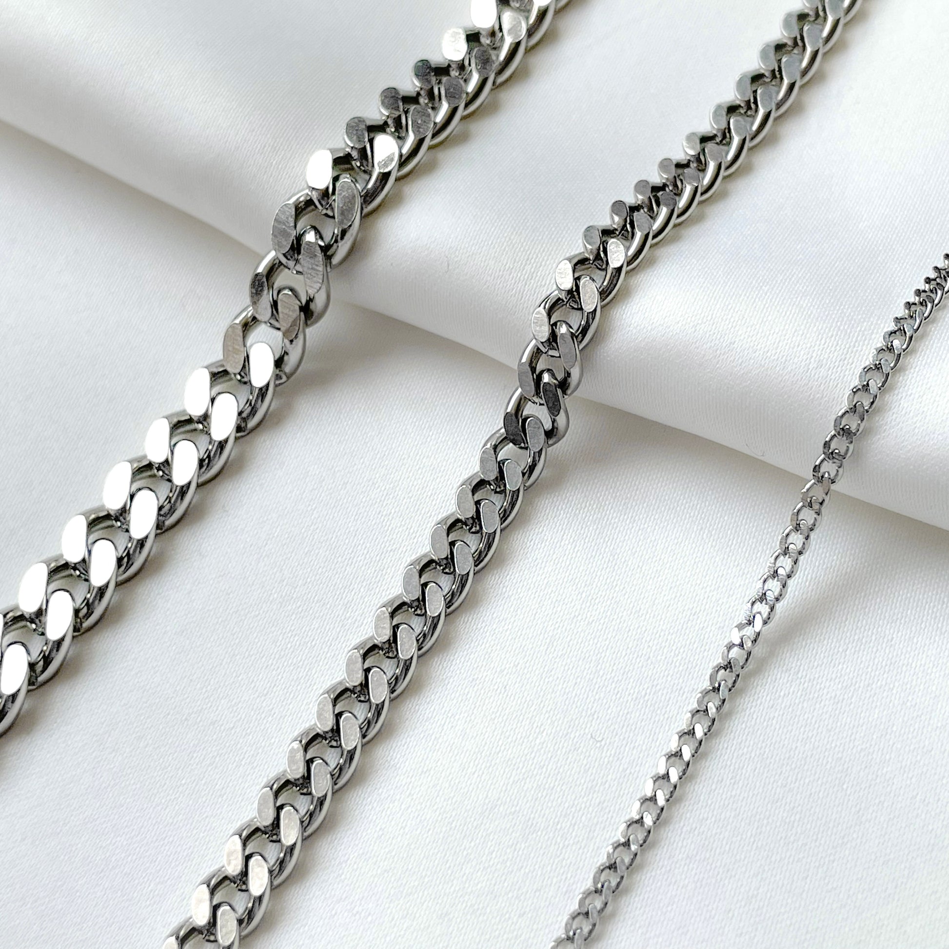 Three silver cuban bracelets in various thicknesses on a white fabric background