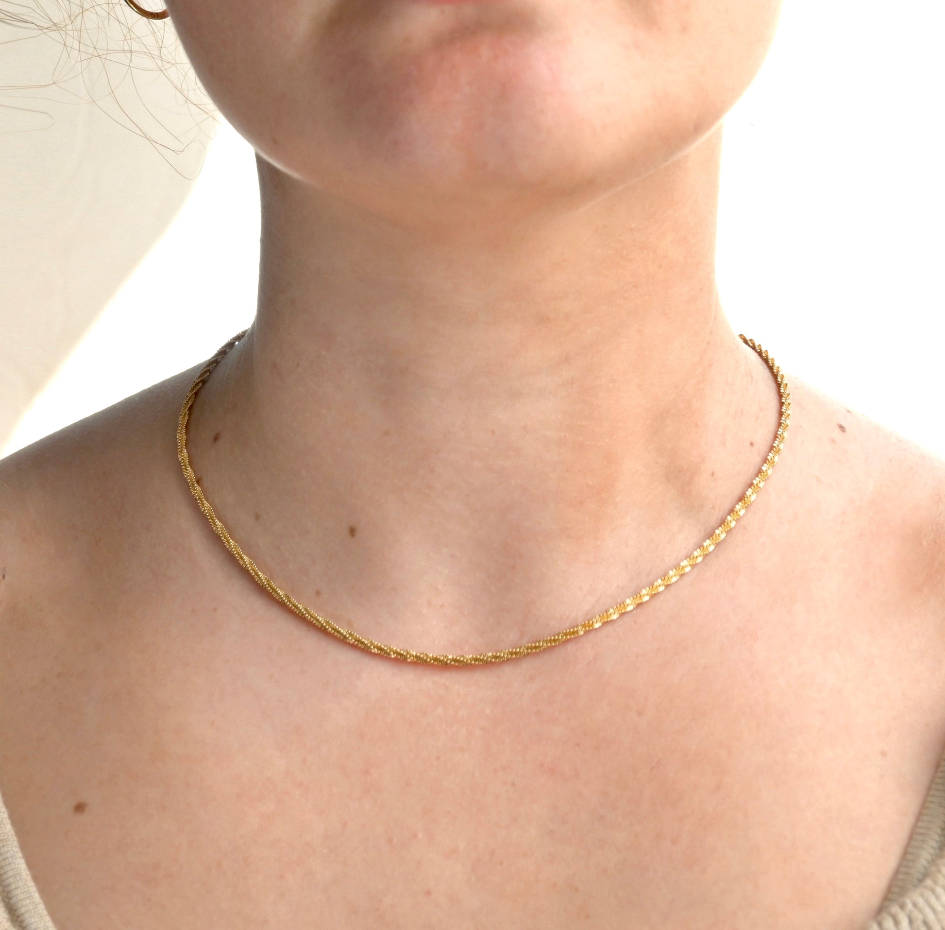 Gold shimmering rope necklace on a person against a neutral background