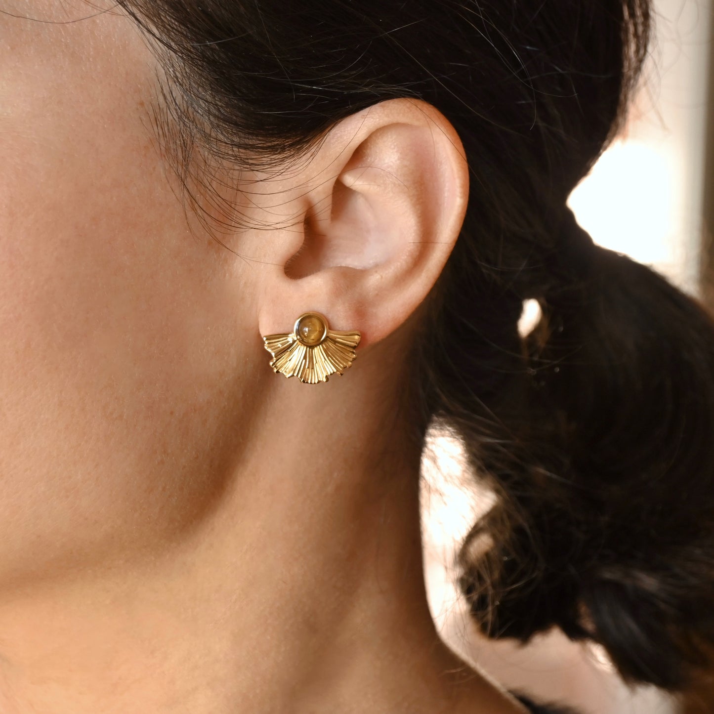 Close-up of a person wearing a gold fan earring with a dark background