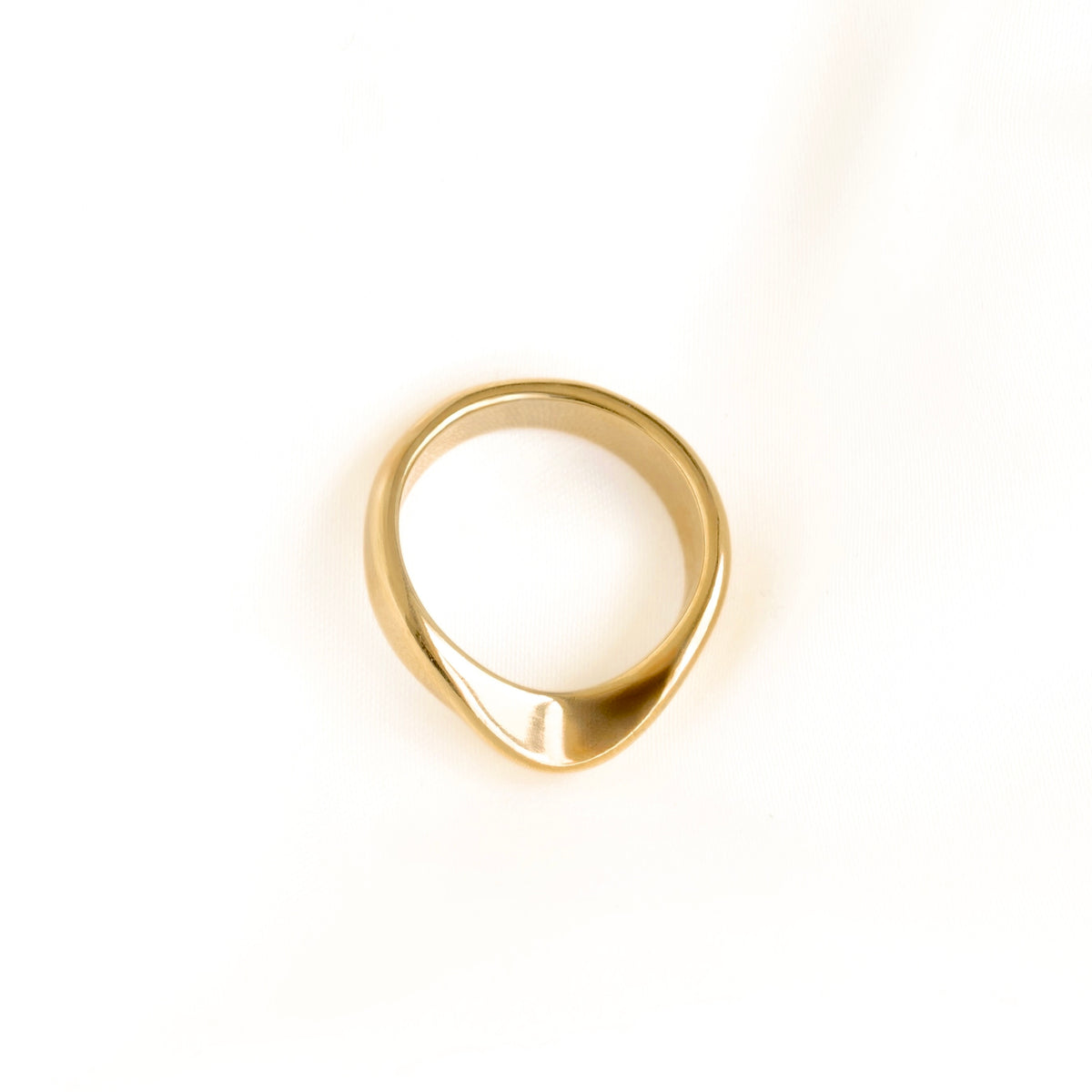 A polished gold ring with a unique, organic wavy shape, photographed from a top-down perspective on a clean white background.