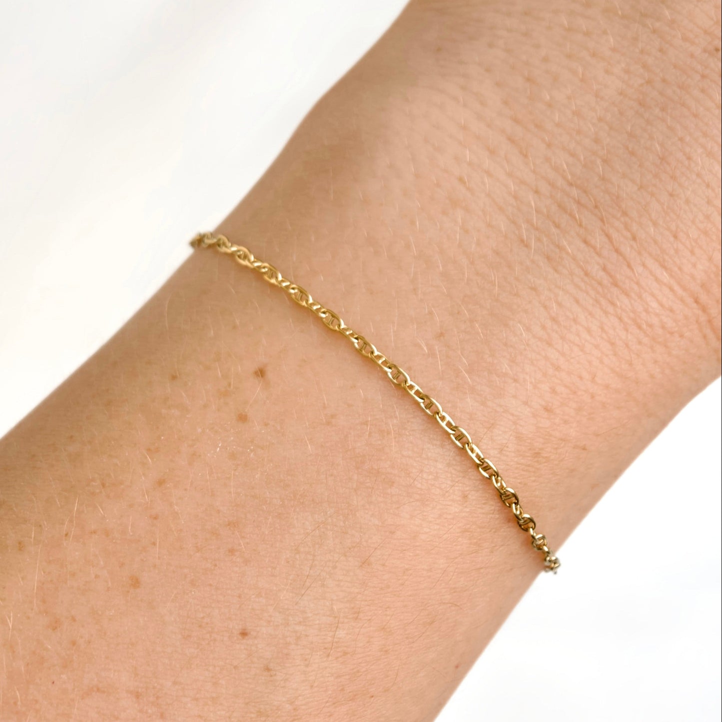 A delicate gold mariner chain bracelet worn on a person's wrist against a clean white background.