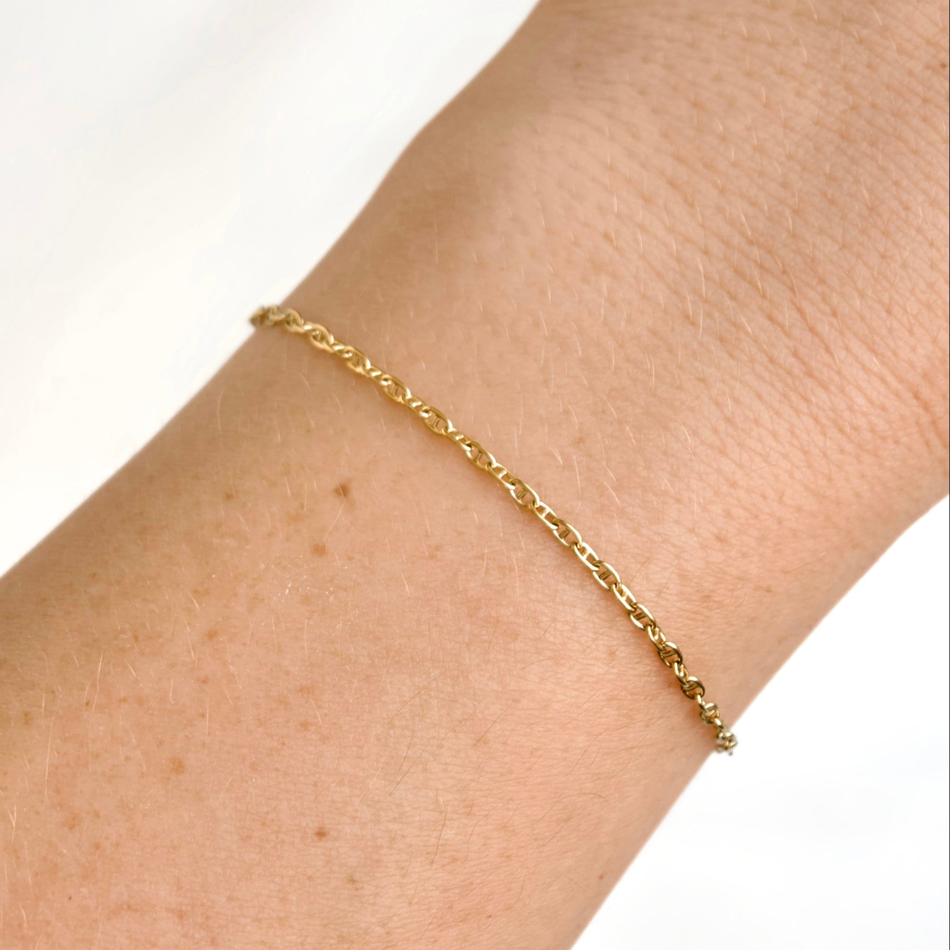 A delicate gold mariner chain bracelet worn on a person's wrist against a clean white background.