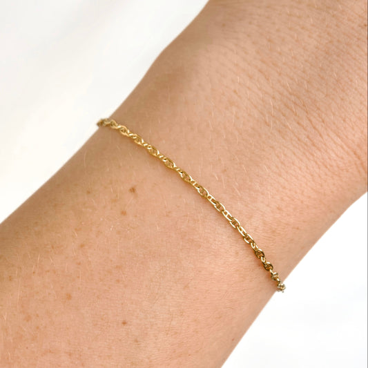 A delicate gold mariner chain bracelet worn on a person's wrist against a clean white background.