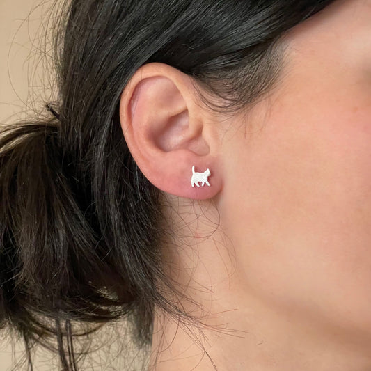 Person wearing silver walking cat stud earrings on a neutral background