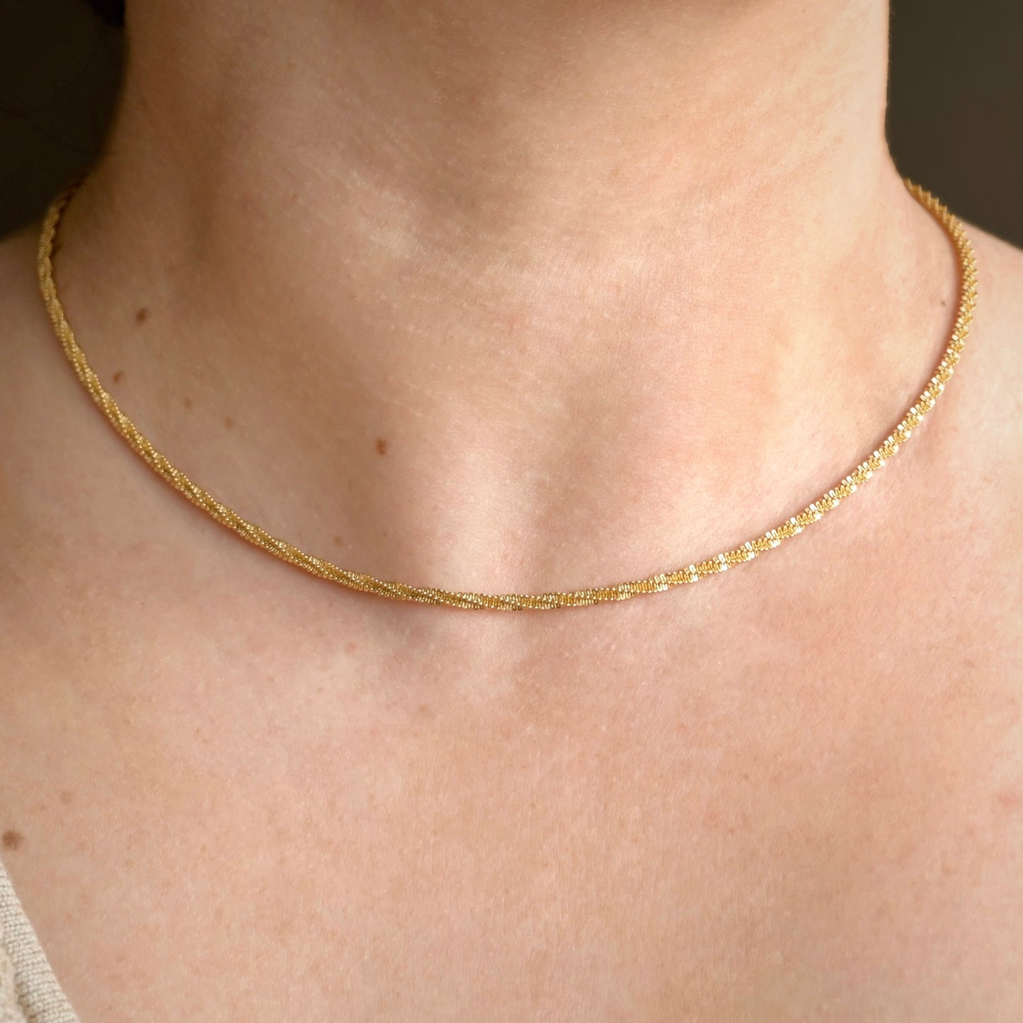 Dainty gold chain on a person's neck with a neutral background