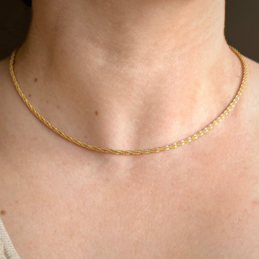 Dainty gold chain on a person's neck with a neutral background