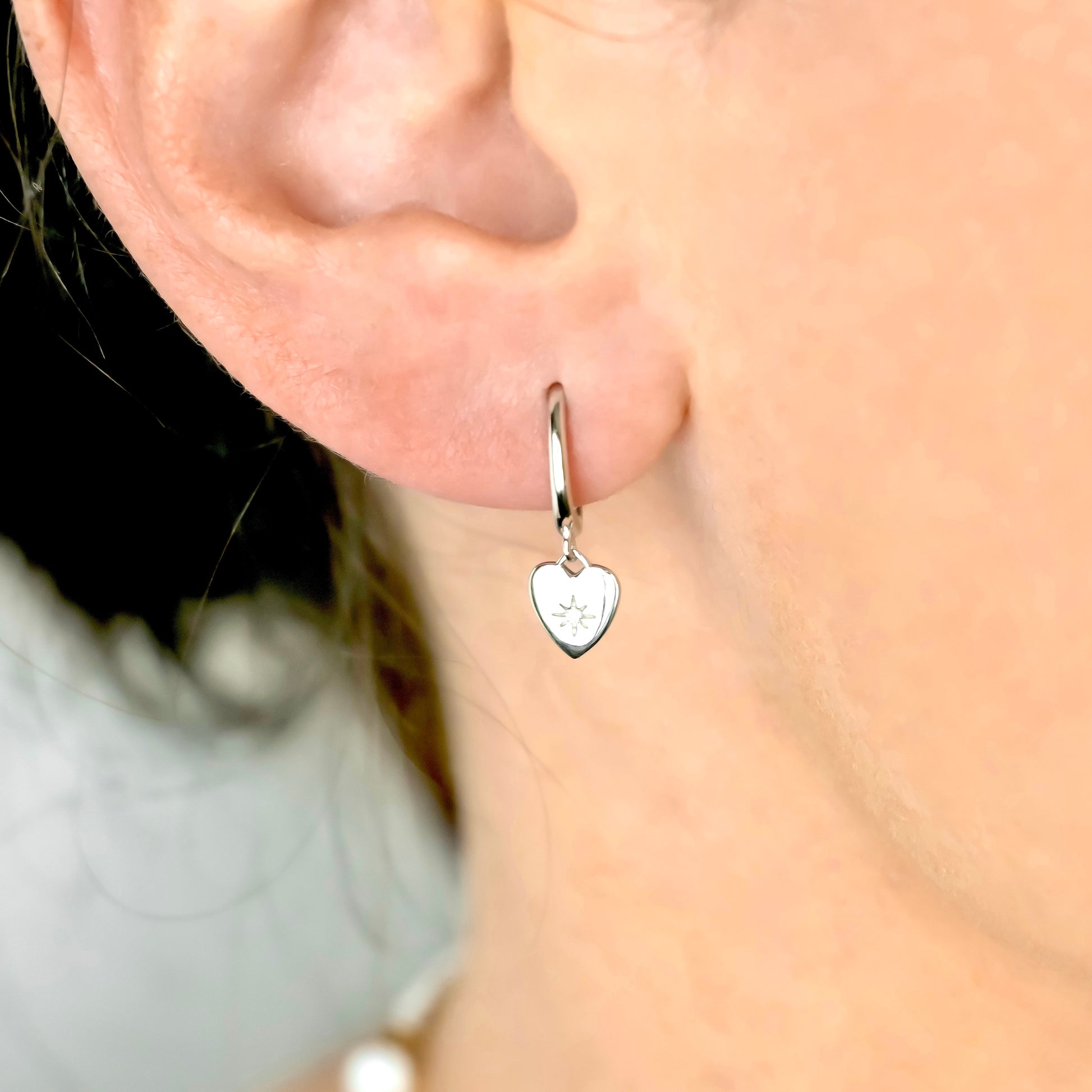 Silver heart-shaped earring worn on an ear with a blurred background