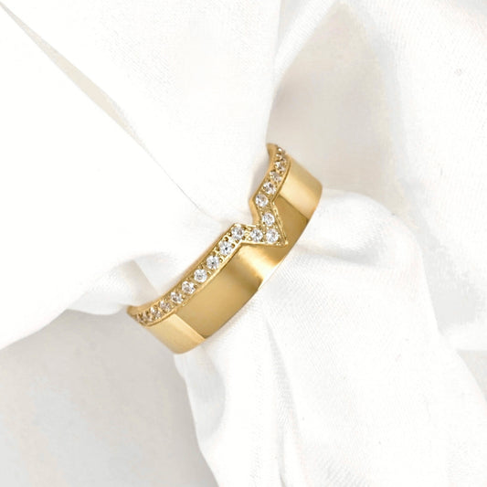 A gold ring with a chevron design, featuring a row of clear pavé stones on one side, displayed on a white fabric napkin.