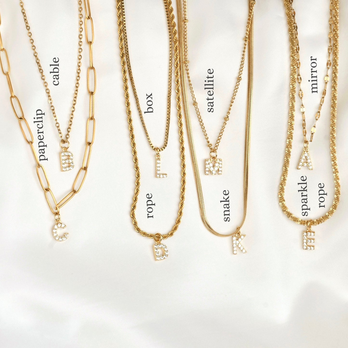 Gold necklaces with various chains including paperclip, cable, rope, box, satellite, snake, mirror and sparkle rope on a white background