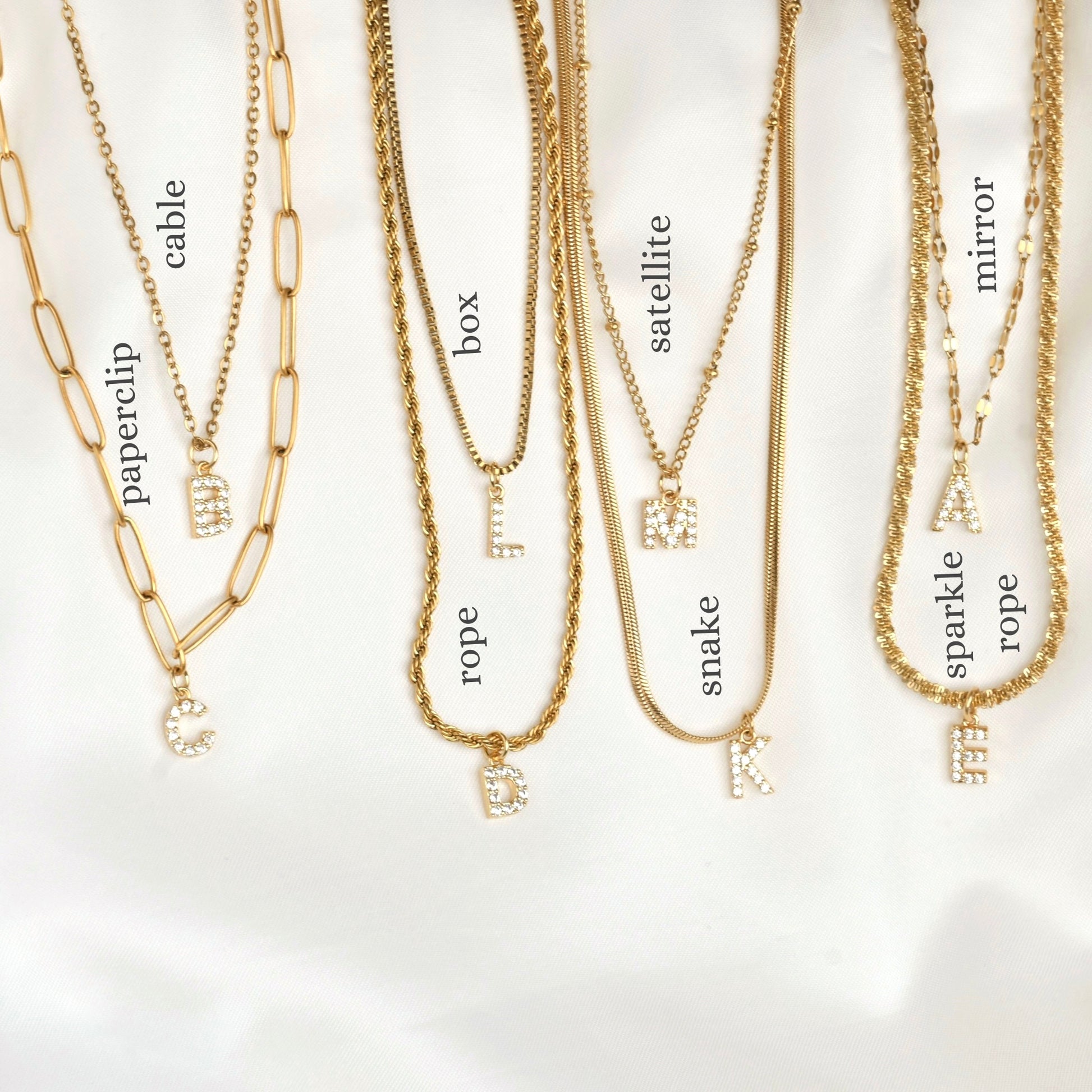 Gold necklaces with various chains including paperclip, cable, rope, box, satellite, snake, mirror and sparkle rope on a white background