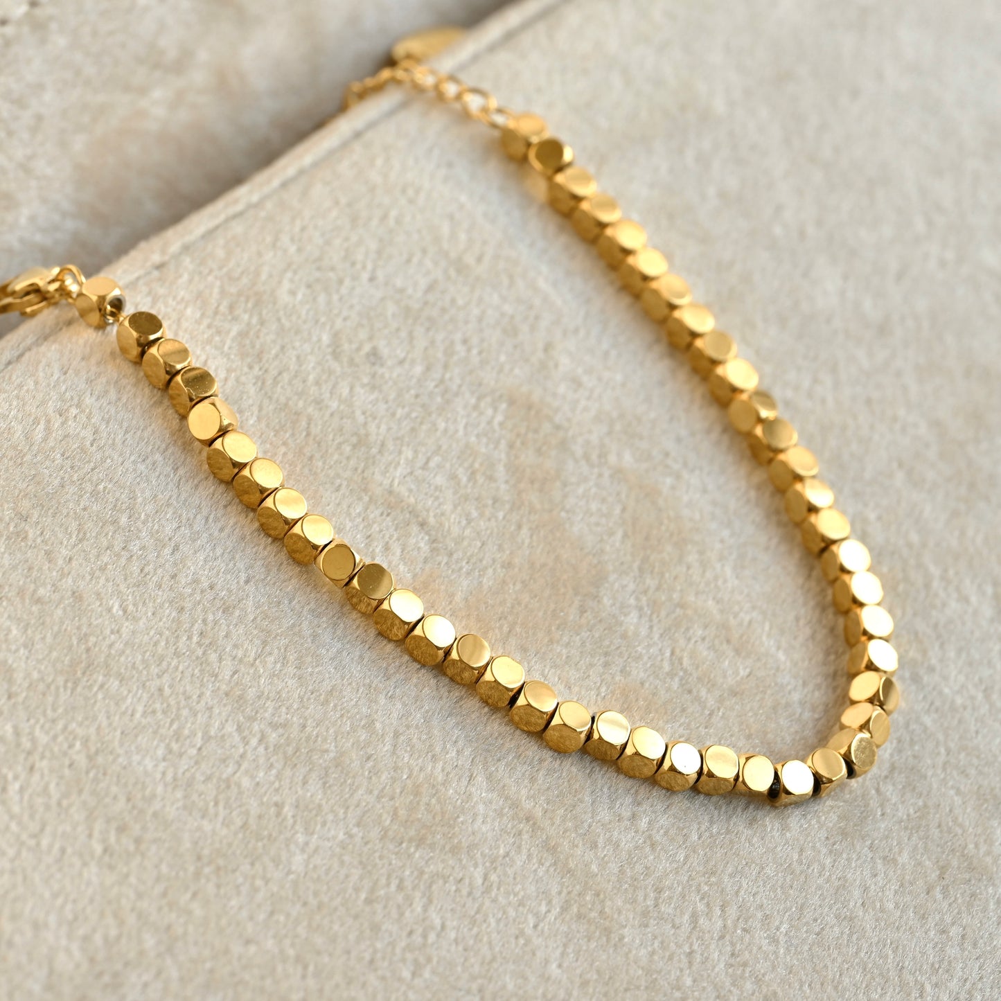 Gold square beaded bracelet on a beige velvet background