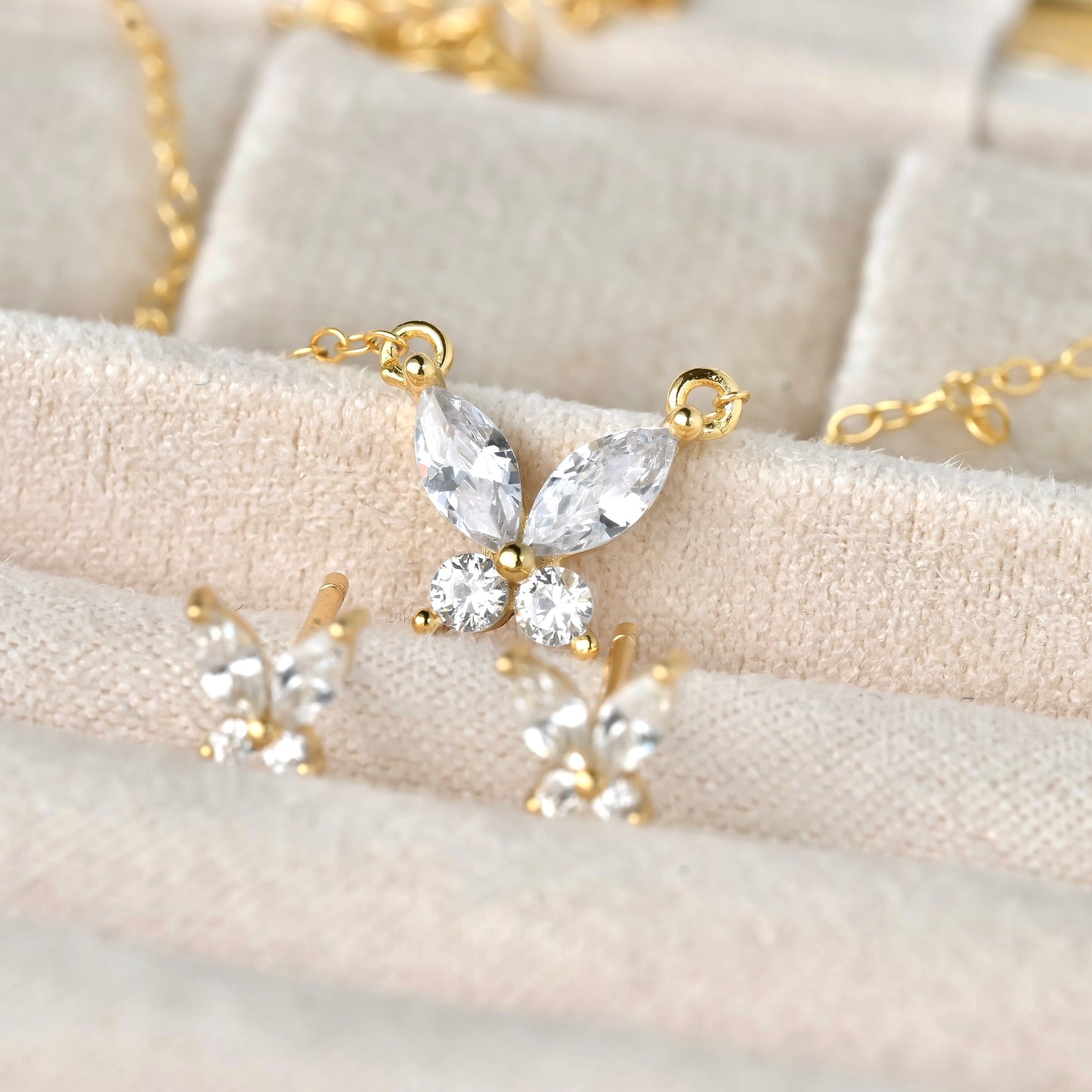 Butterfly-shaped gold and crystal necklace on a textured beige surface
