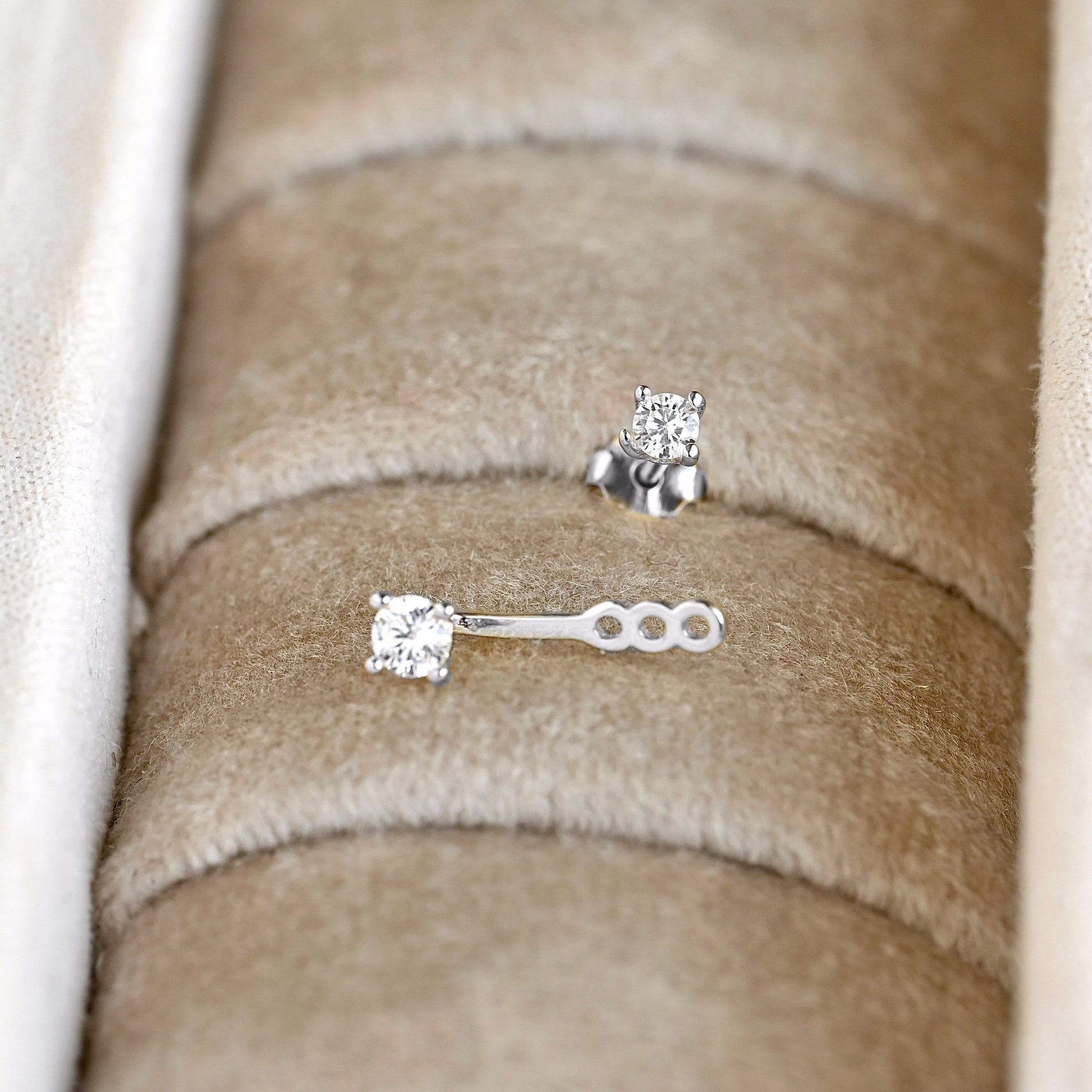 Silver-toned ear jacket with clear CZ stones, one stud with butterfly backing and one jacket style with three slots displayed in a beige jewelry box.
