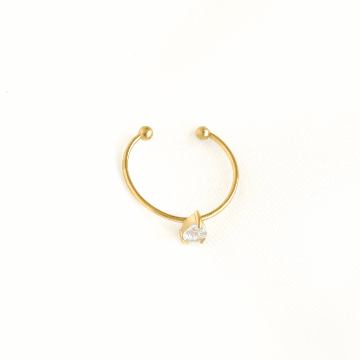 A delicate gold crescent-shaped hoop earring with a small clear heart-shaped gemstone at the center, displayed on a clean white background.