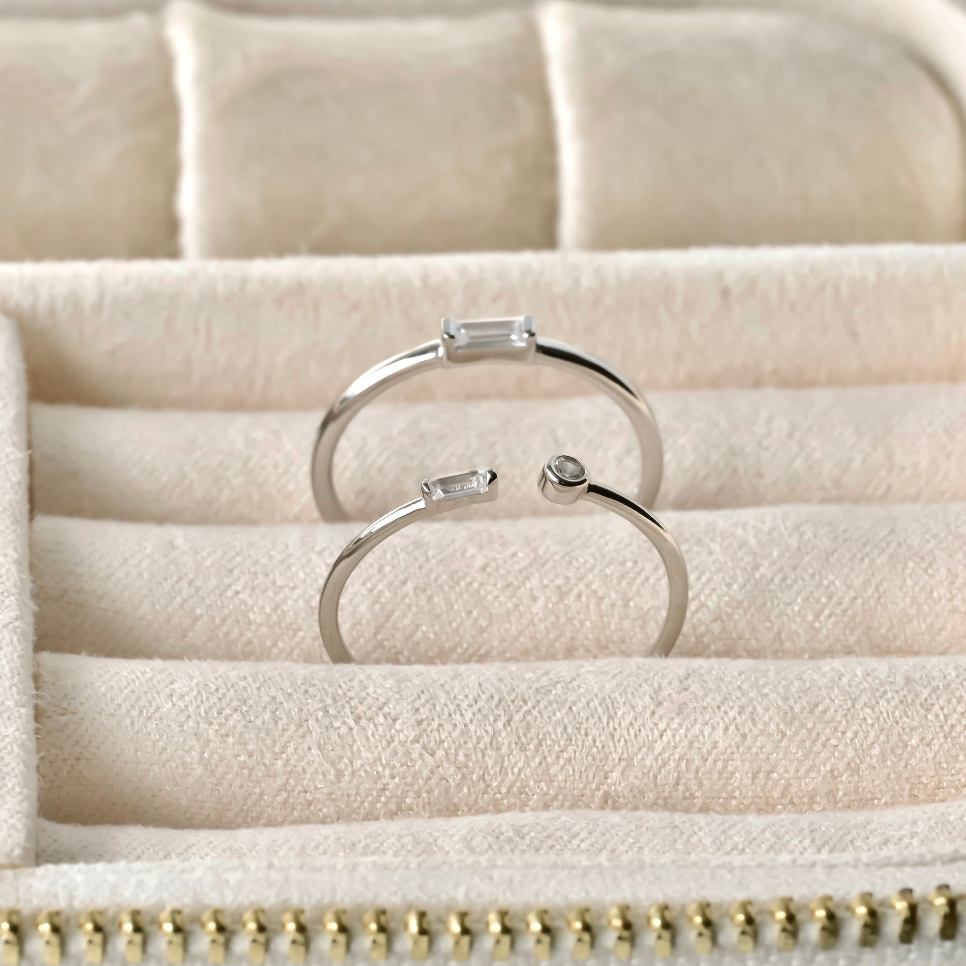 Two silver rings with gemstones on a textured beige surface