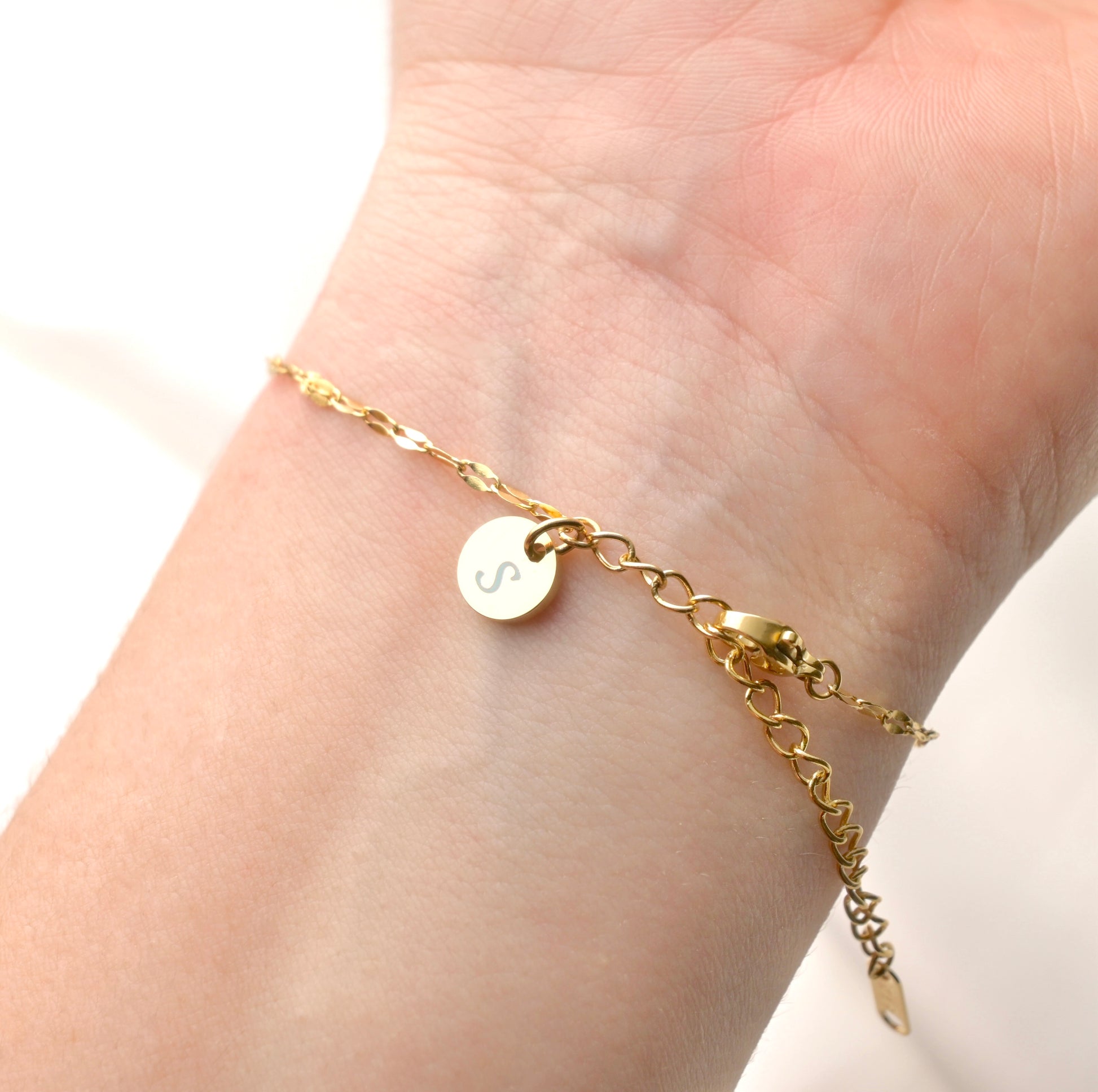 Gold bracelet with a round letter charm on a wrist against a white background