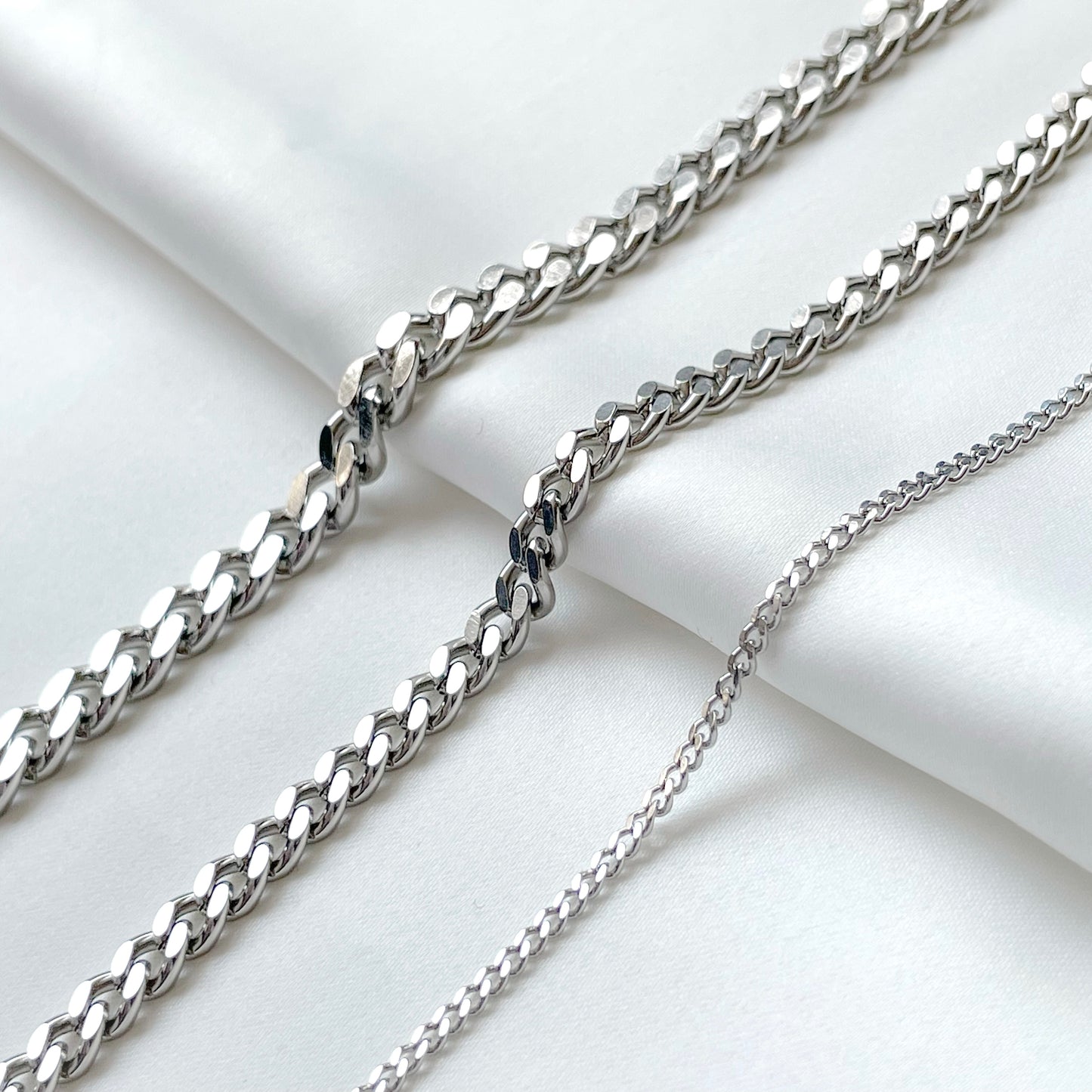 Three silver curb chains of different thicknesses on a light background