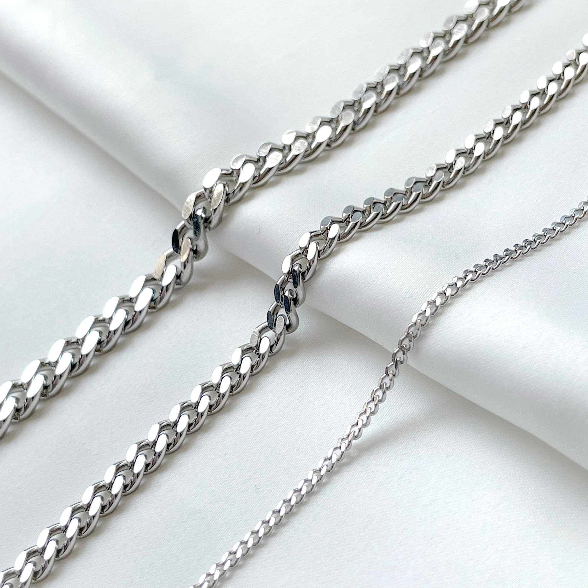 Three silver curb chains of different thicknesses on a light background