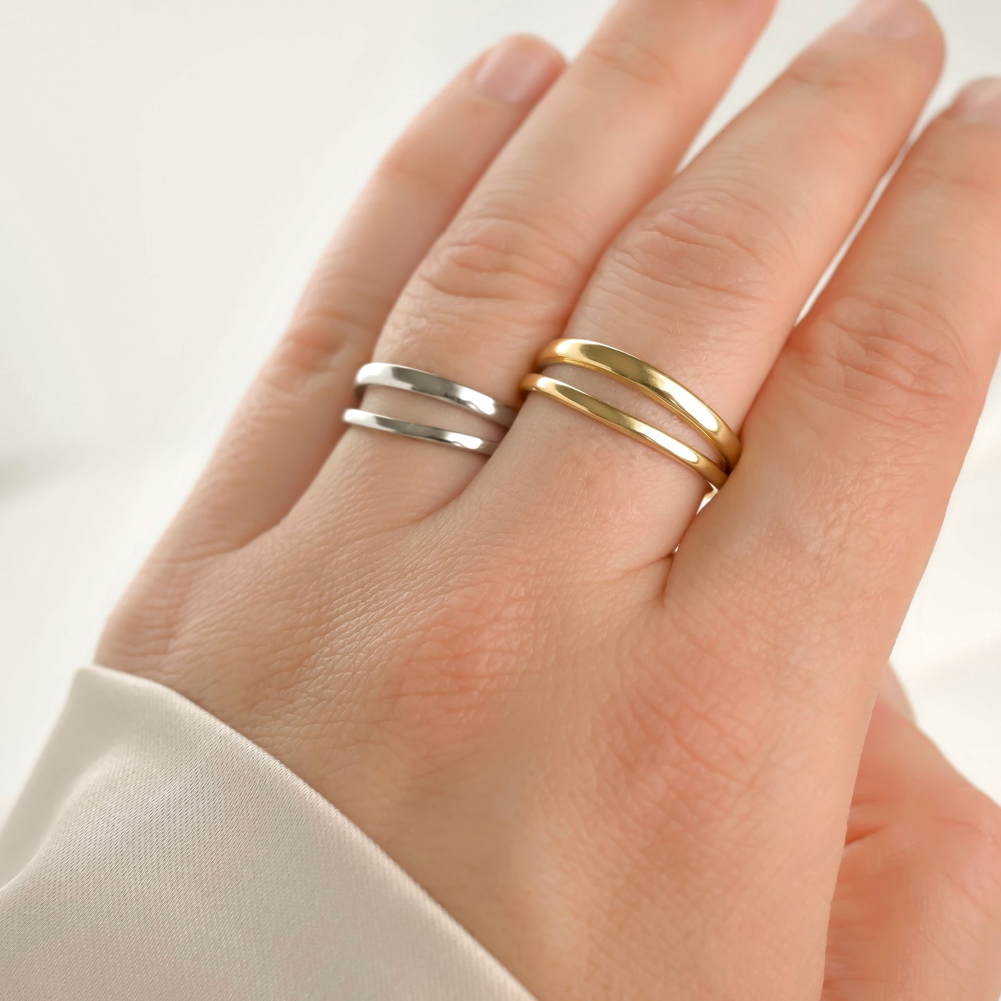 Angled view: Hand wearing two double band rings, one gold and one silver, on a light background