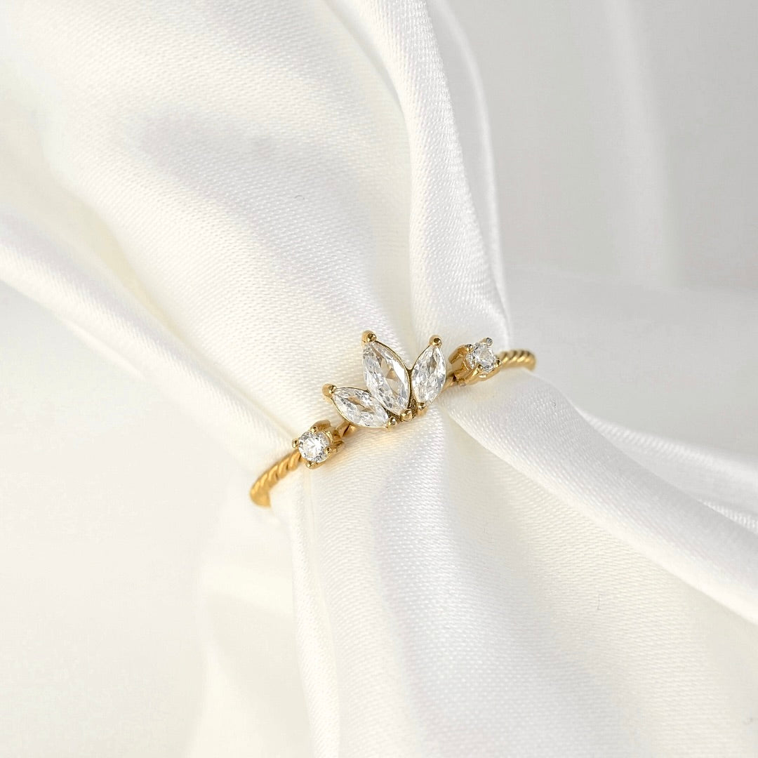 A delicate gold twisted ring with marquise-cut clear gemstones arranged in a leaf-like cluster, displayed on draped white satin fabric.